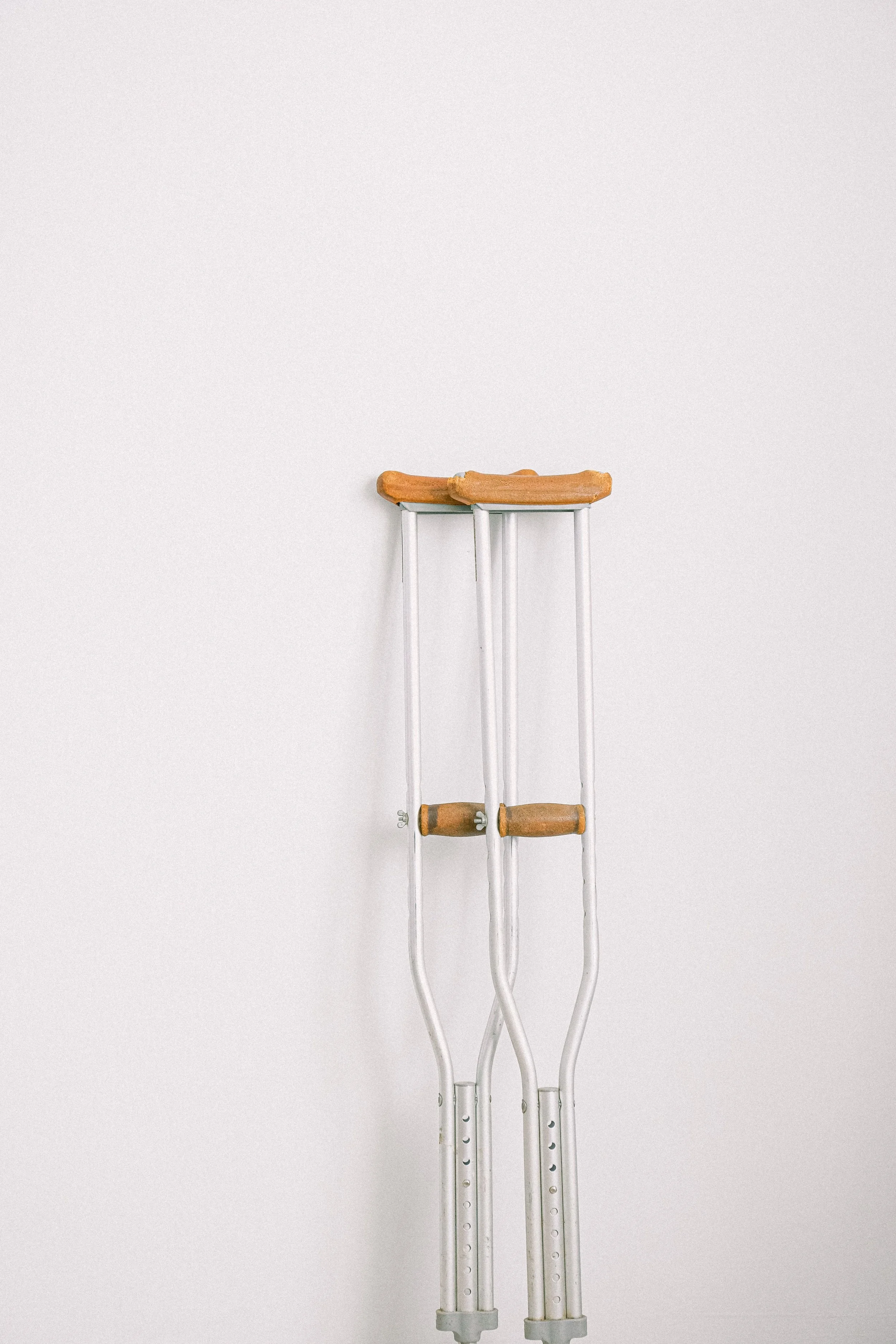 Pair of crutches with wooden handles and white metal frames against a plain light background.