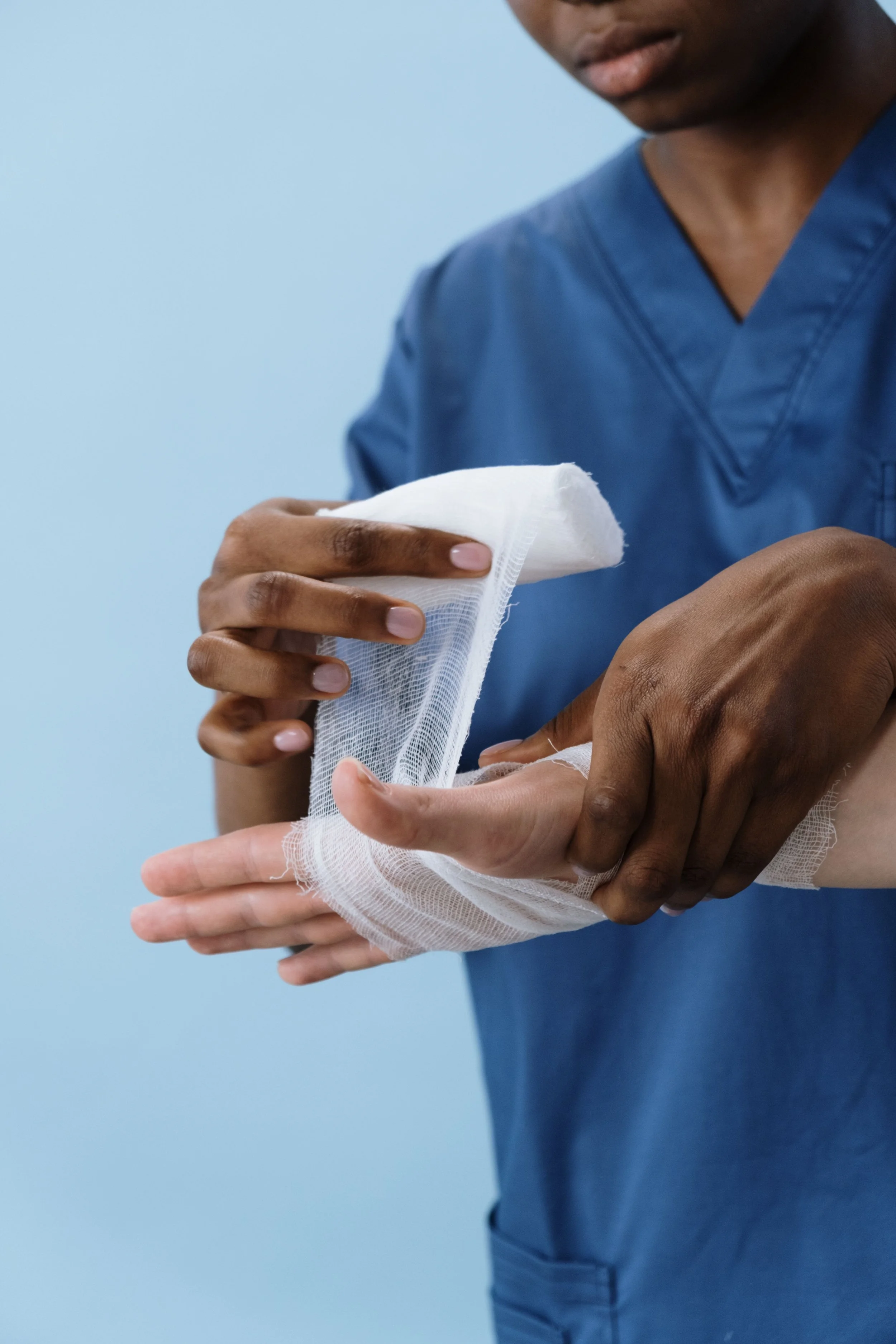 A person dressed in medical scrubs wrapping a bandage around their arm.