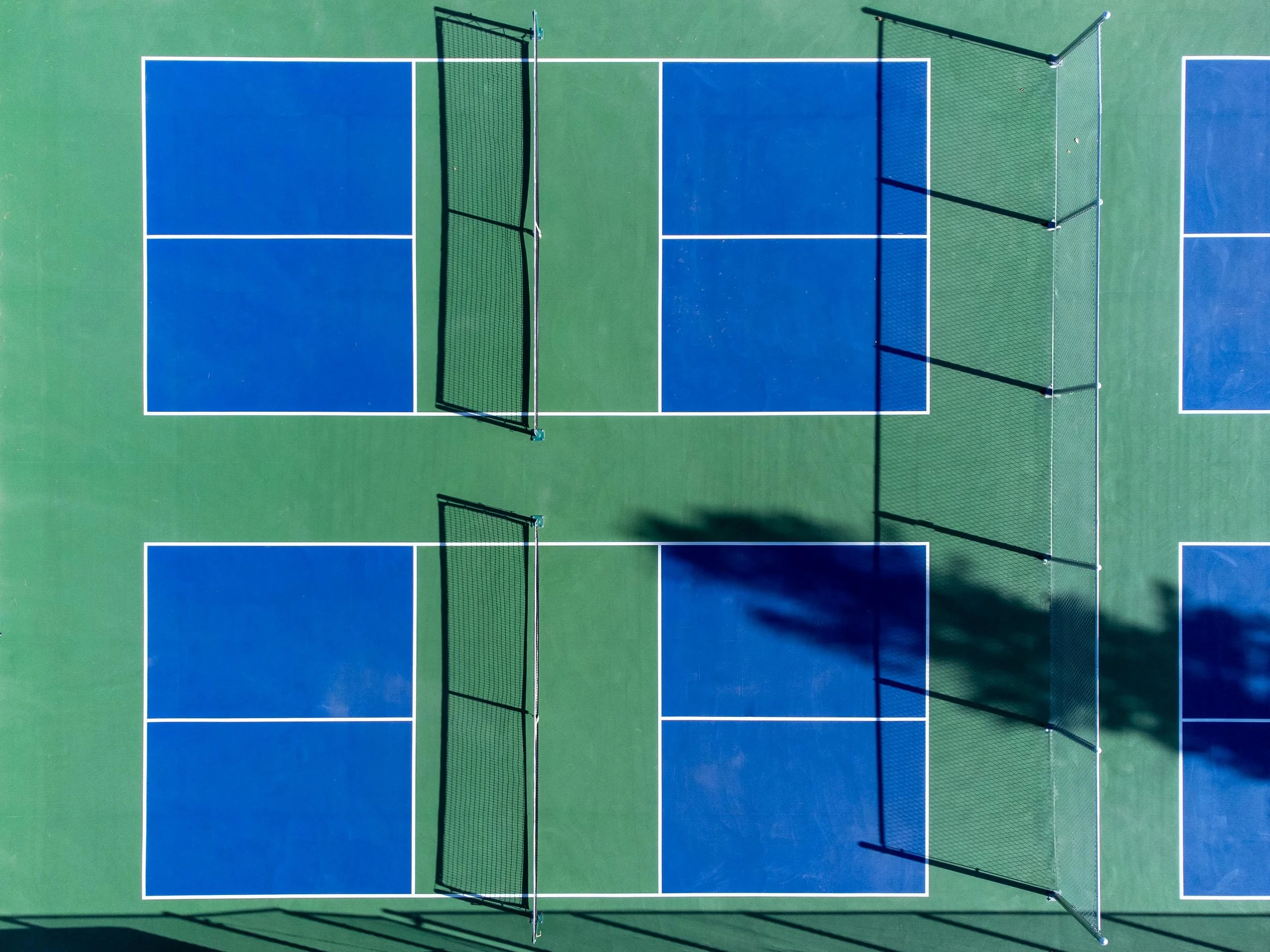 Overhead view of a blue and green outdoor pickleball or tennis court with nets.