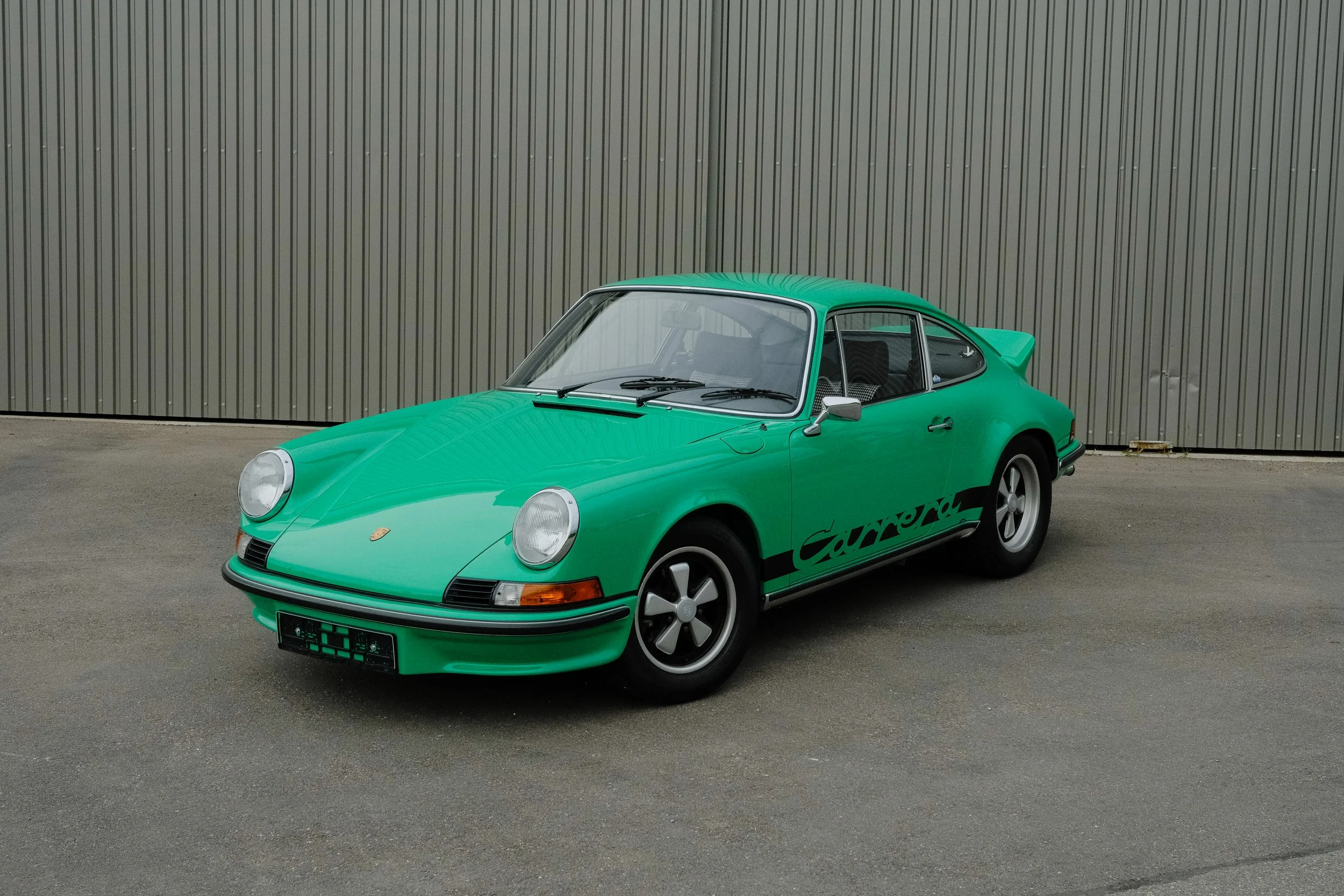Original 1973 Porsche 911 Carrera RS 2.7 in rare Mint Green, shown from the front three-quarter angle with black Carrera side graphics and Fuchs wheels.