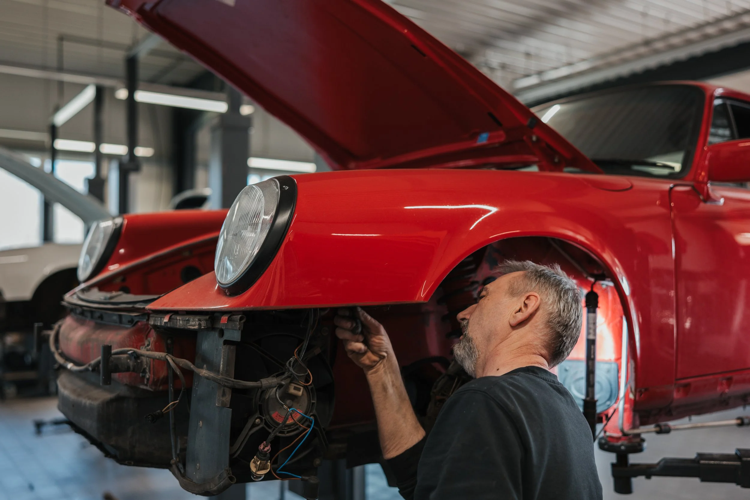 A partially assembled vintage red Porsche 911 in a garage, with the front and rear wheels removed and elevated on wooden pallets, surrounded by tools and equipment.