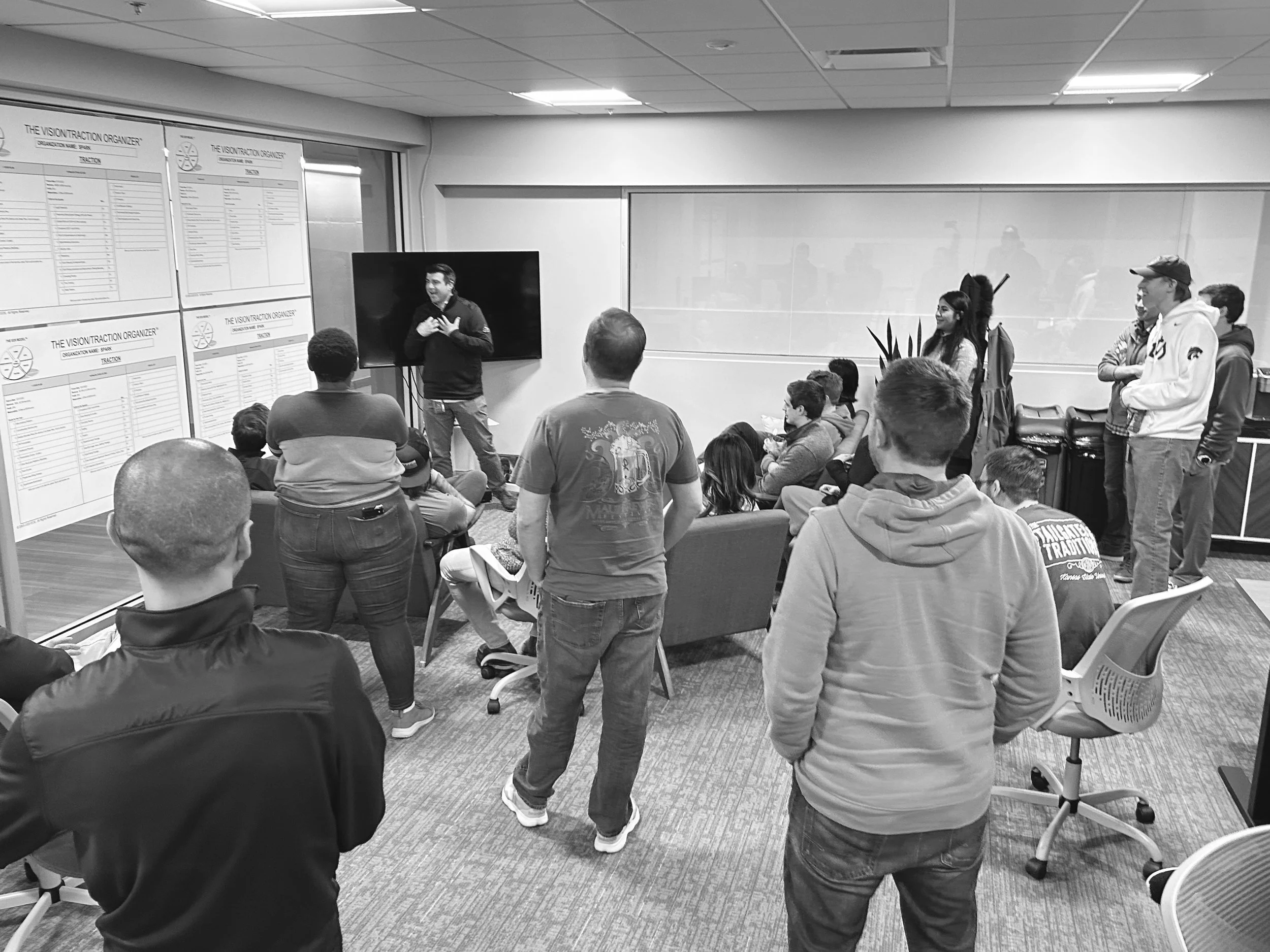 Group of people attending a presentation in a conference room with a man speaking in front of a screen.