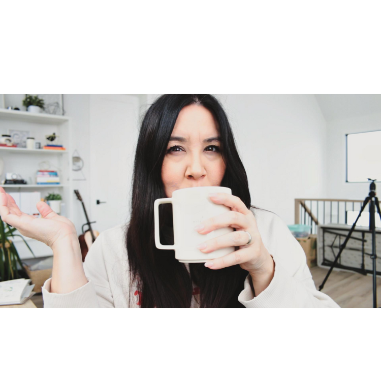 Woman with dark hair sipping from a white mug in a bright, modern room.