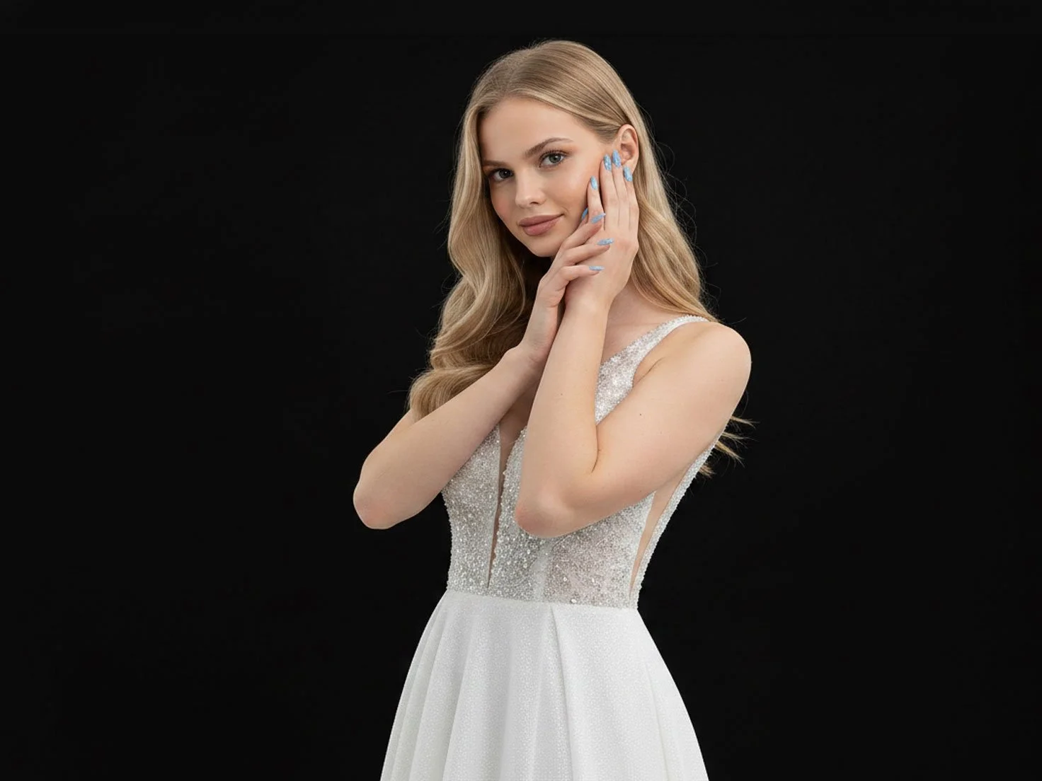A woman with long blonde hair poses against a black background, wearing a white, beaded evening gown with a deep V-neckline and her Gel X nail design touching her face.