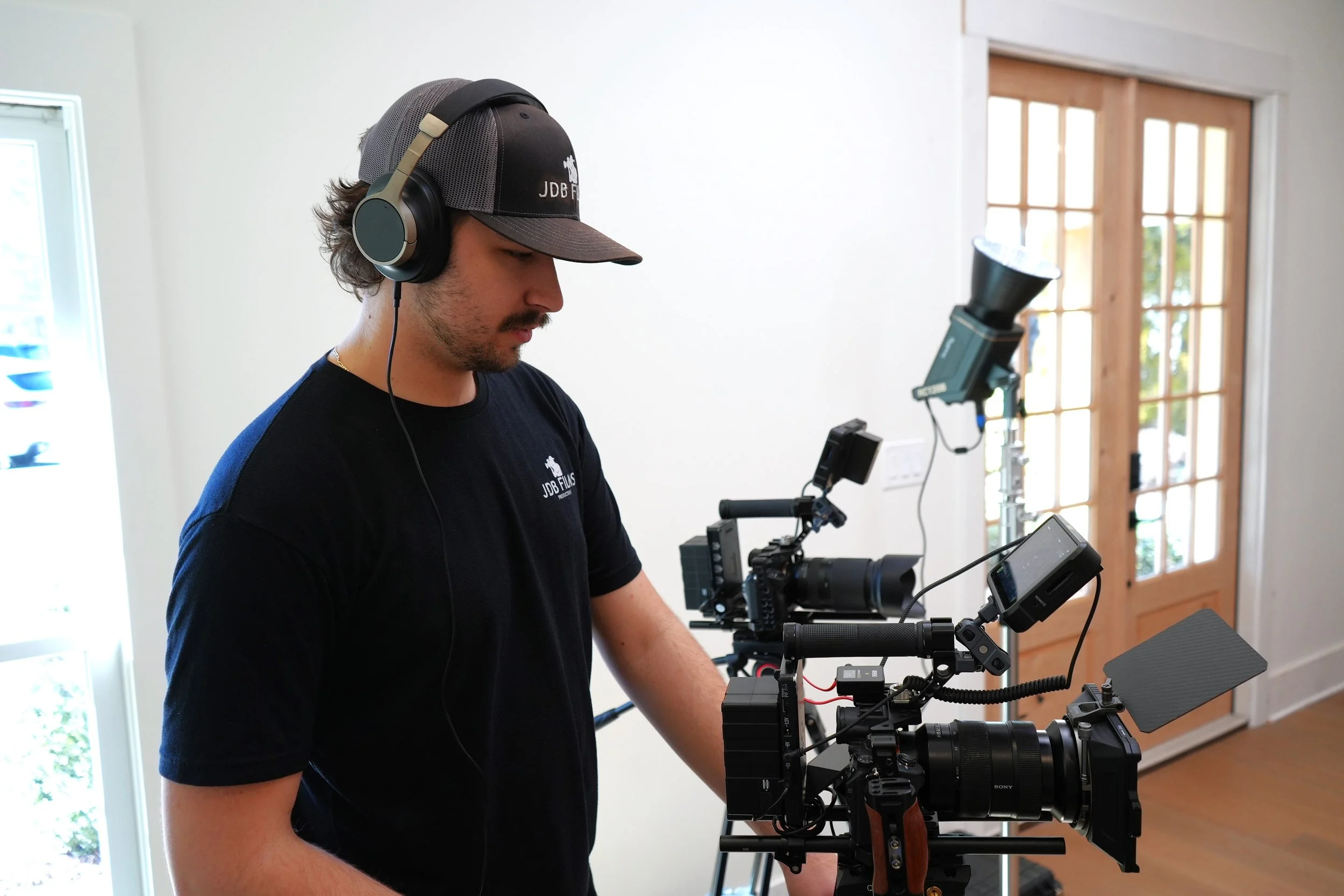 A man wearing headphones and a cap operating a professional camera setup indoors.