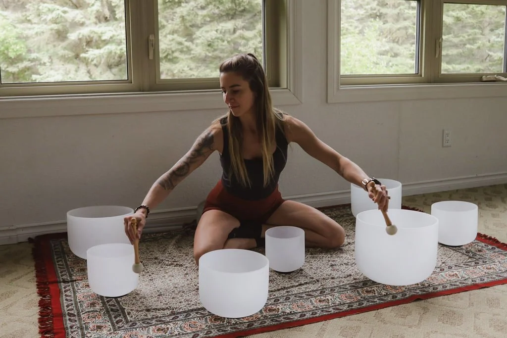 A woman sitting on the floor playing crystal bowls for a sound bath experience on a yoga retreat.