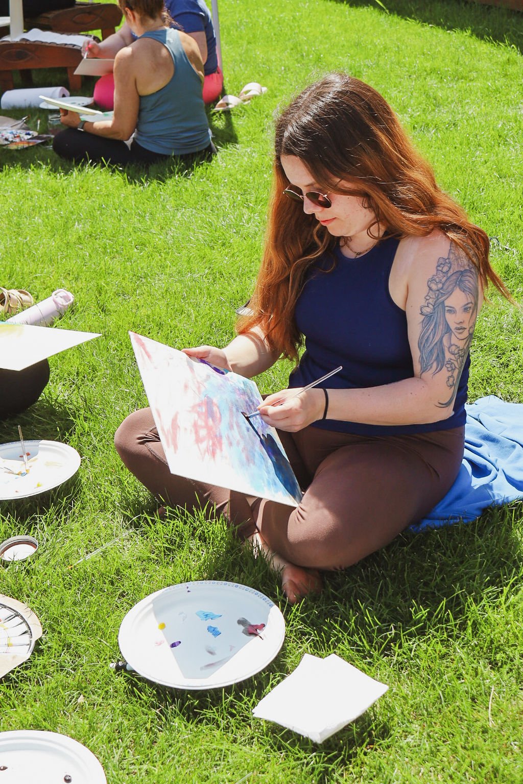 Woman sitting in the grass painting on a beautiful day at a yoga retreat.