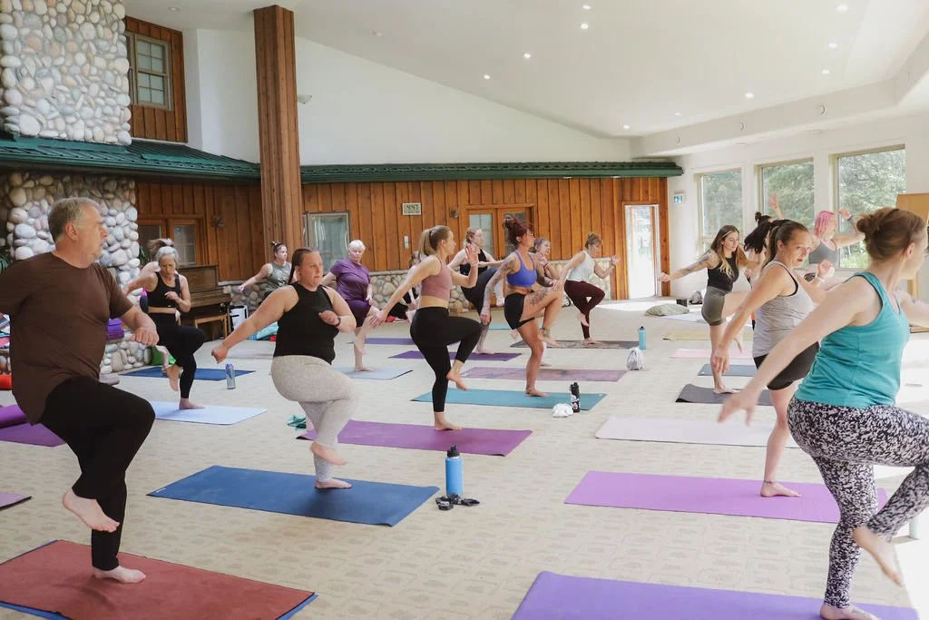 A group of people in an open room doing yoga driving one knee up.
