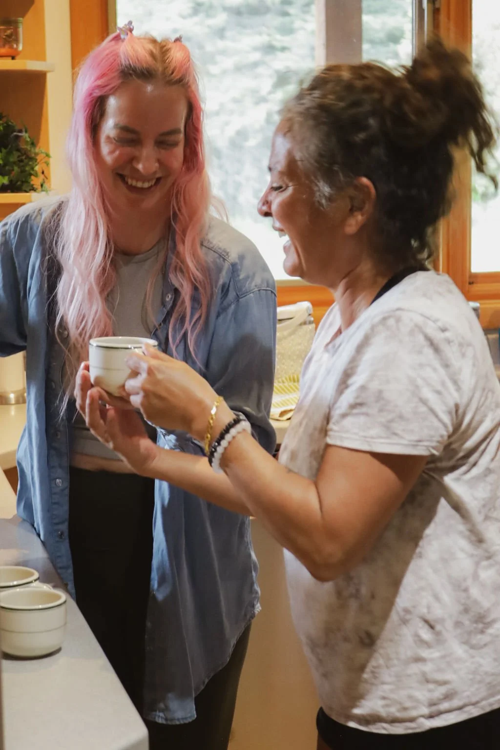 Two women laughing while drinking tea together.