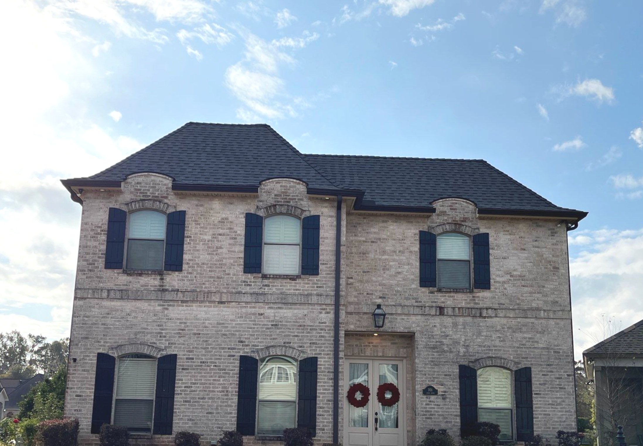 Brick house with six windows, dark shutters, and Christmas wreaths on the front door.