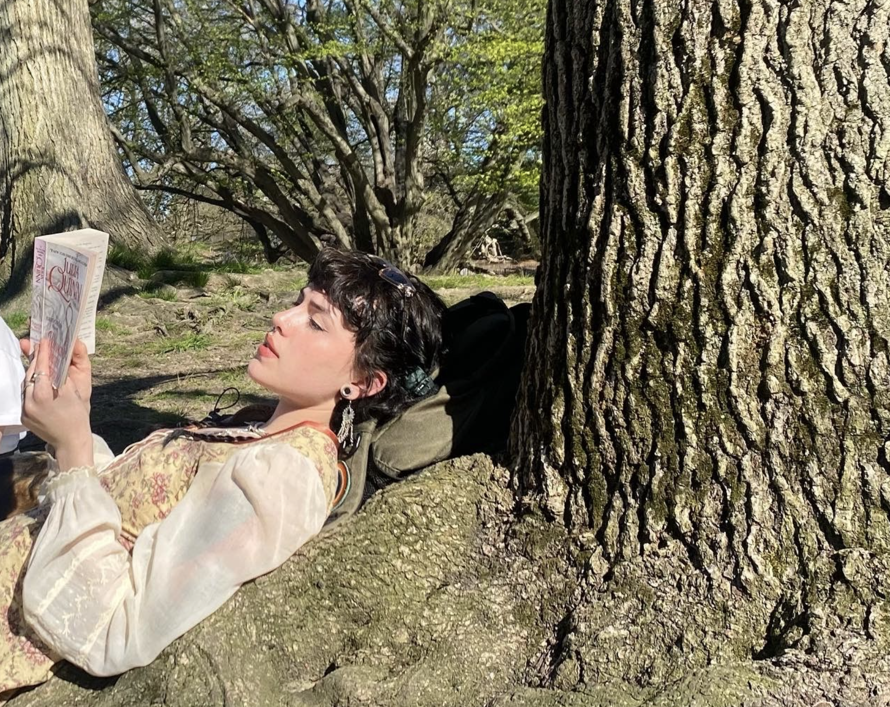 Thursdae leaning against a tree while reading a book