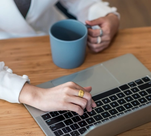 Person typing on a laptop with a blue mug nearby.