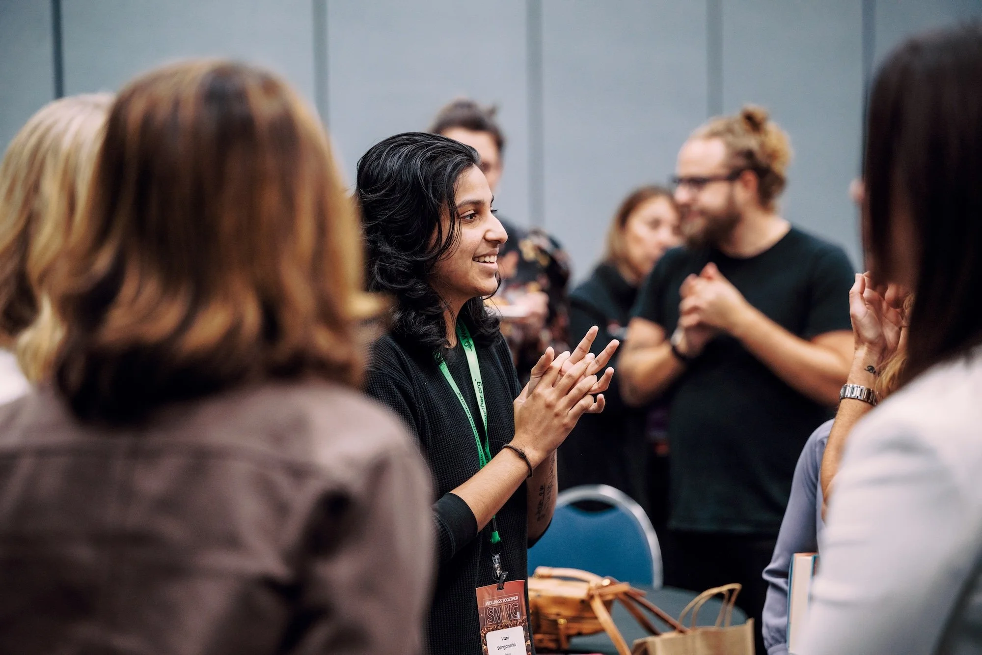 A woman speaking at a conference, wearing a burgundy dress, with a conference badge around her neck, standing in front of a podium with a laptop, at the 8th Annual Wellness Together Conference.
