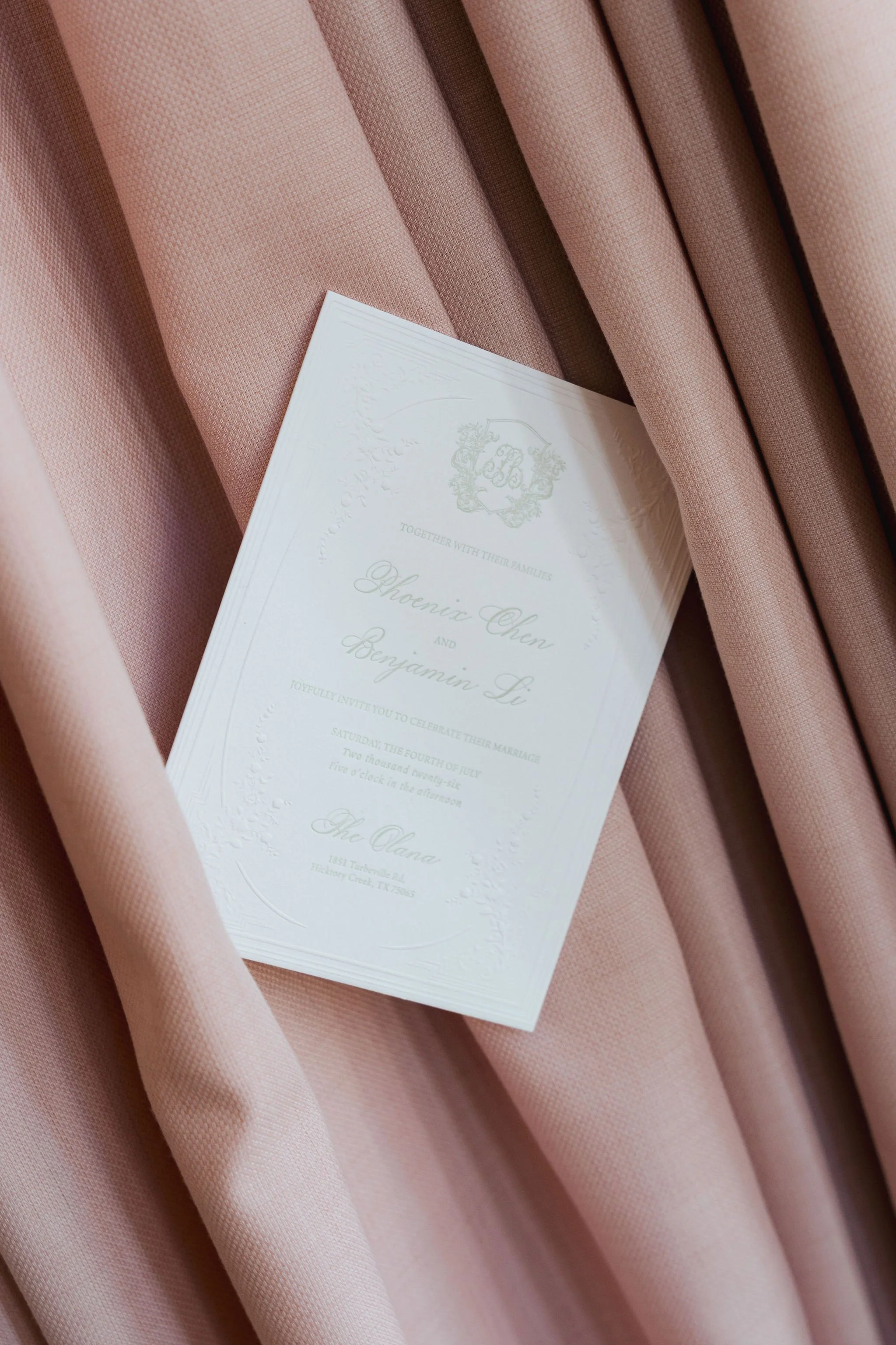 A pink textured fabric background with a white wedding invitation card partially placed on top.