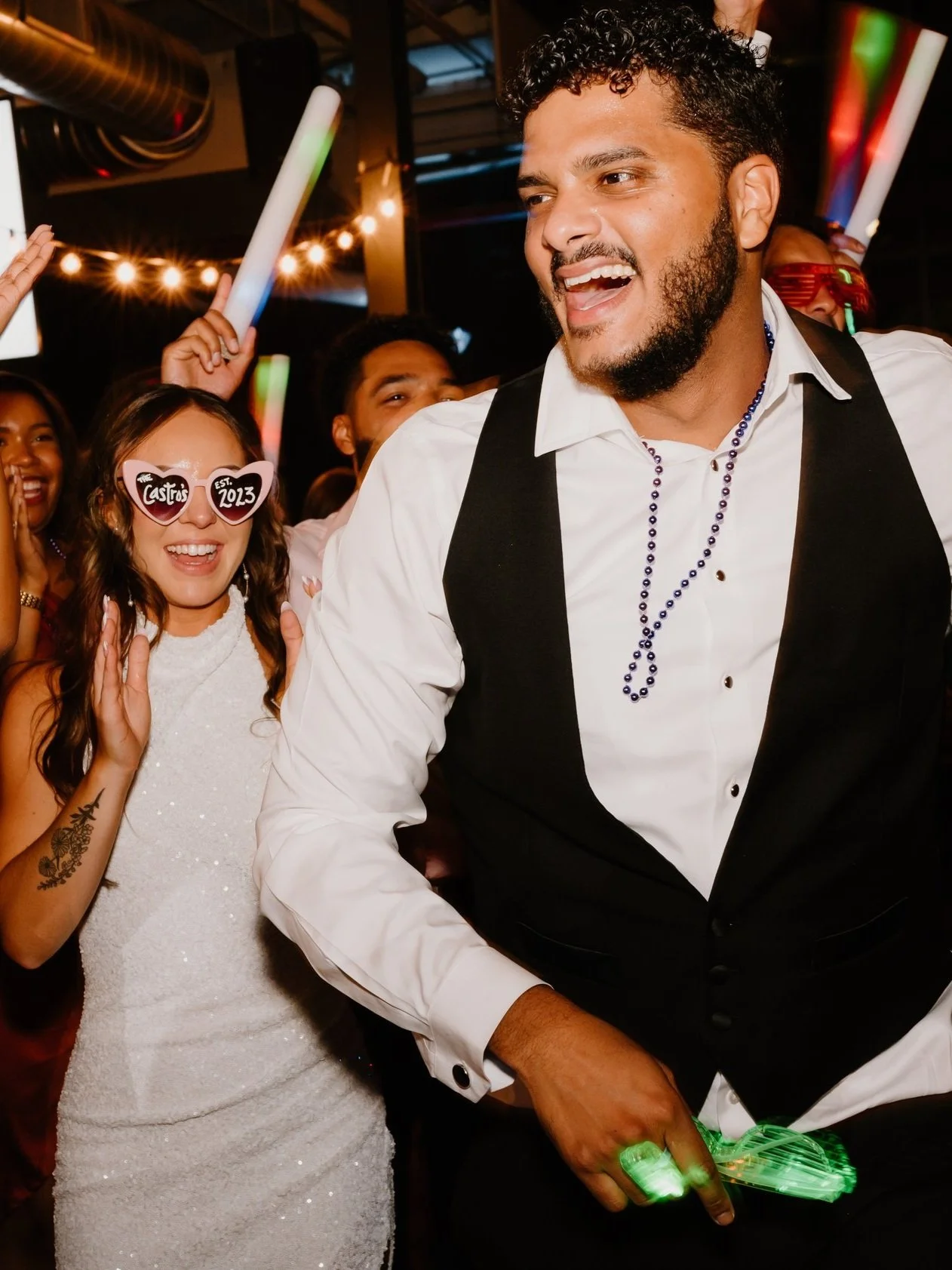 Group of people celebrating at a weddin, some with glow sticks, wearing festive attire, and smiling.