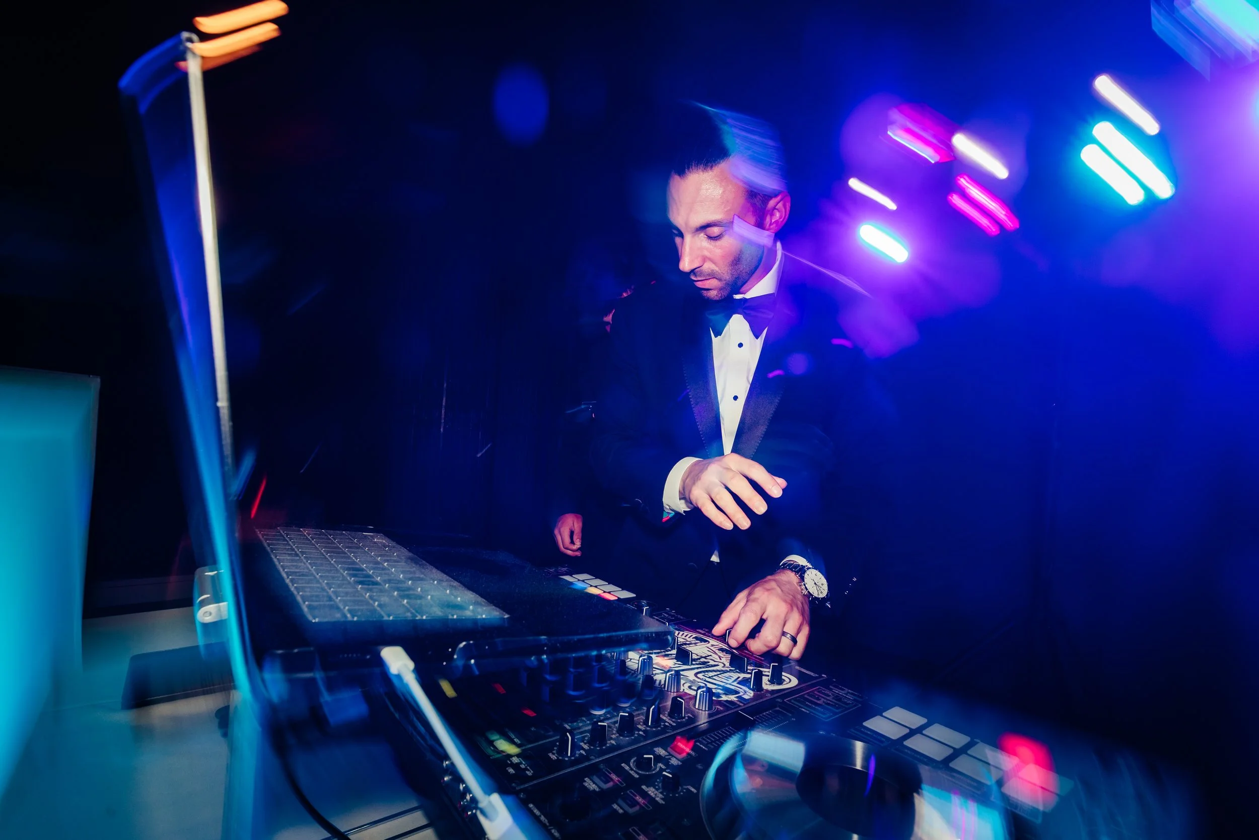 DJ with headphones in a suit, mixing music at a nightclub with colorful lights and DJ equipment.