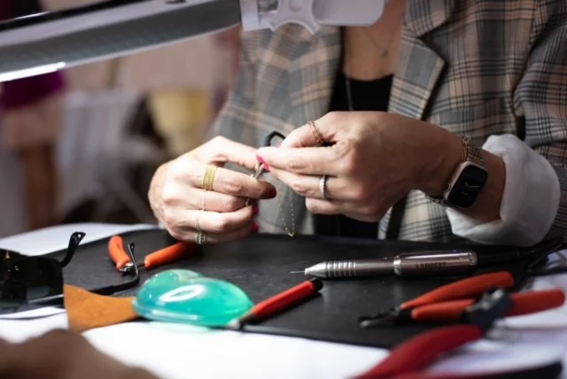 Person working on jewelry with various tools on a black work mat.