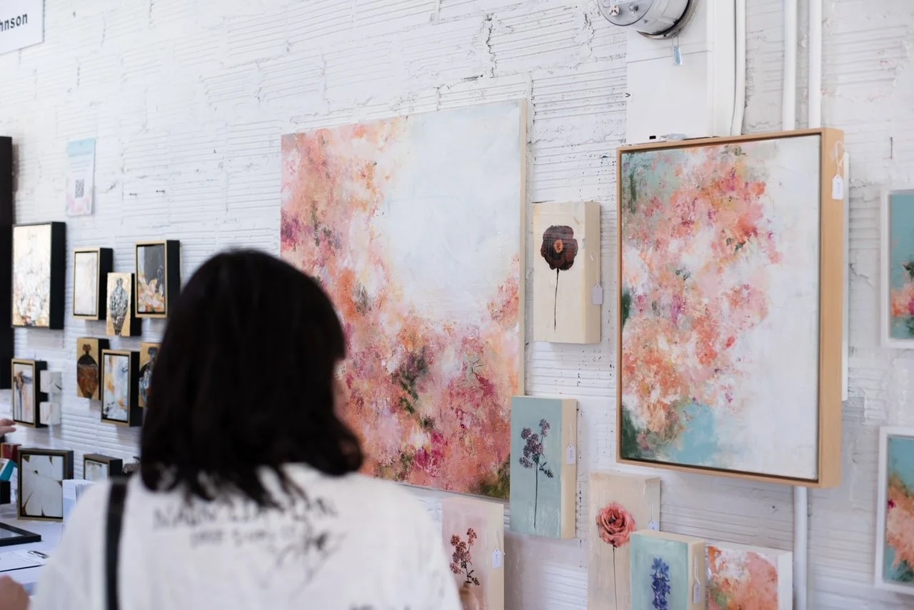 Person viewing abstract floral paintings at an art gallery.