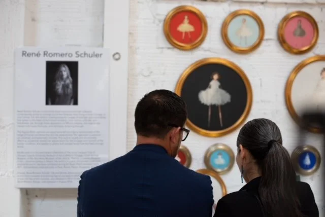 A man and woman viewing ballet-themed artwork on a white wall with framed pictures of ballet dancers.