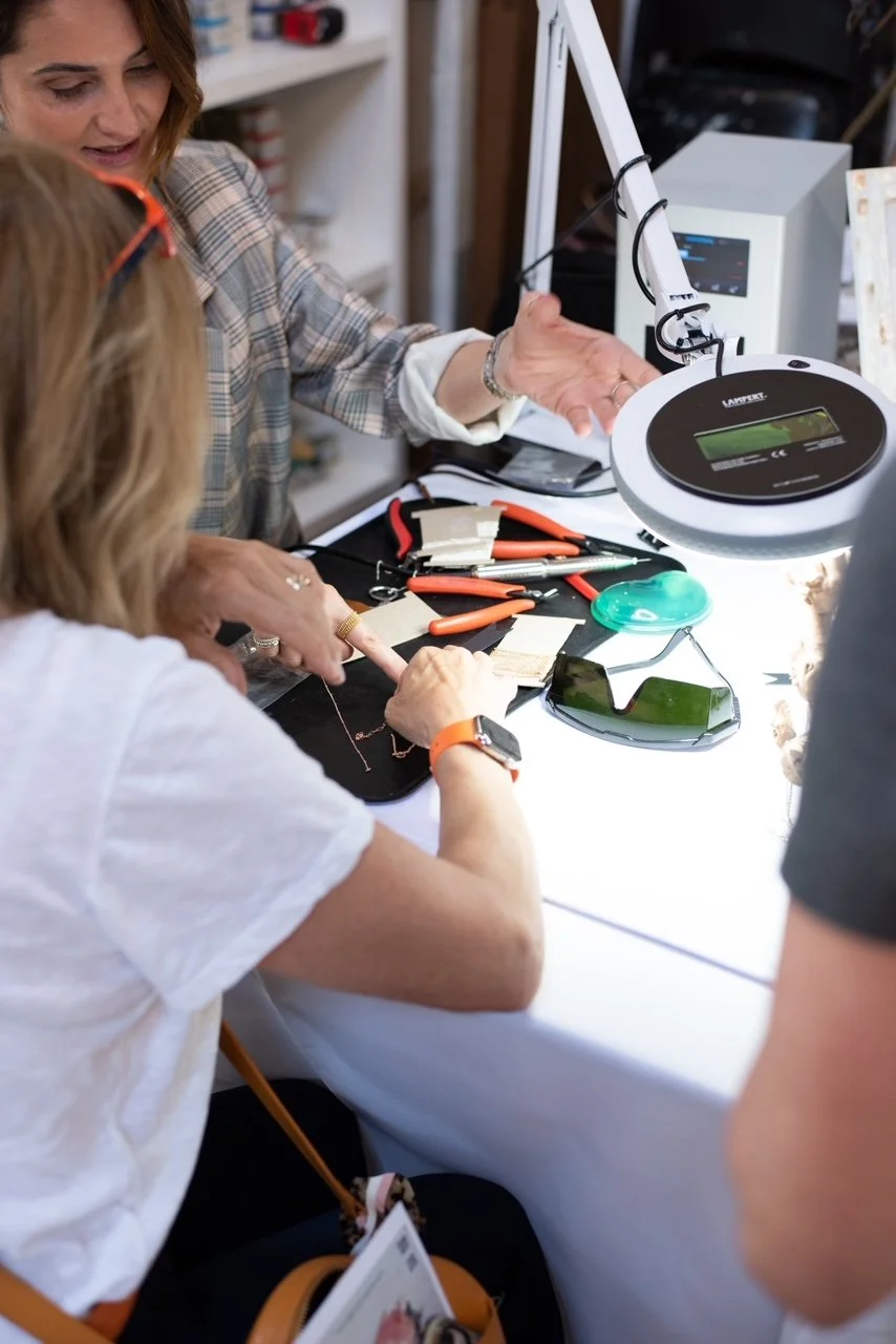 People working on jewelry at a workspace with tools, jewelry pieces, and magnifying glasses.