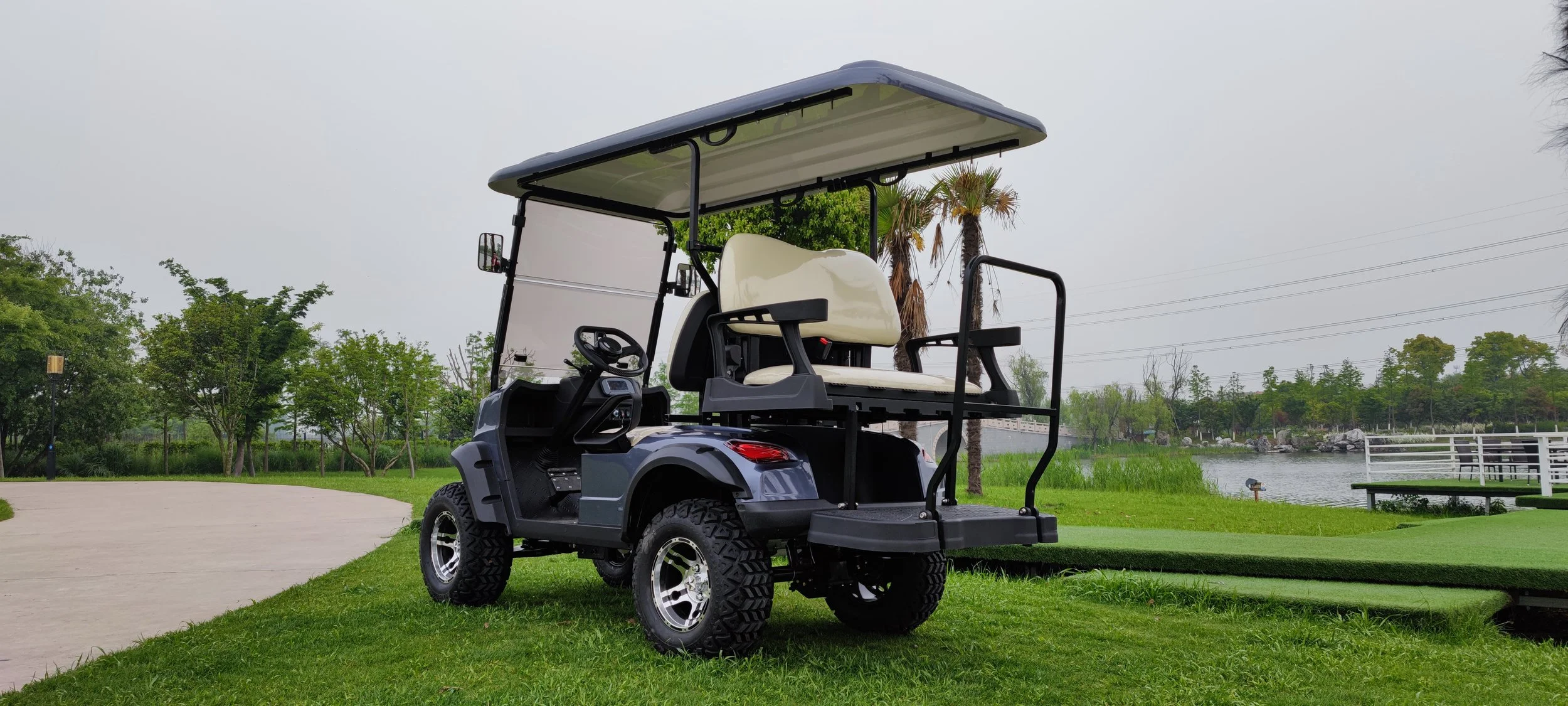 A black golf cart with beige seats parked on grass beside a golf course, near a pond and trees, under a cloudy sky.
