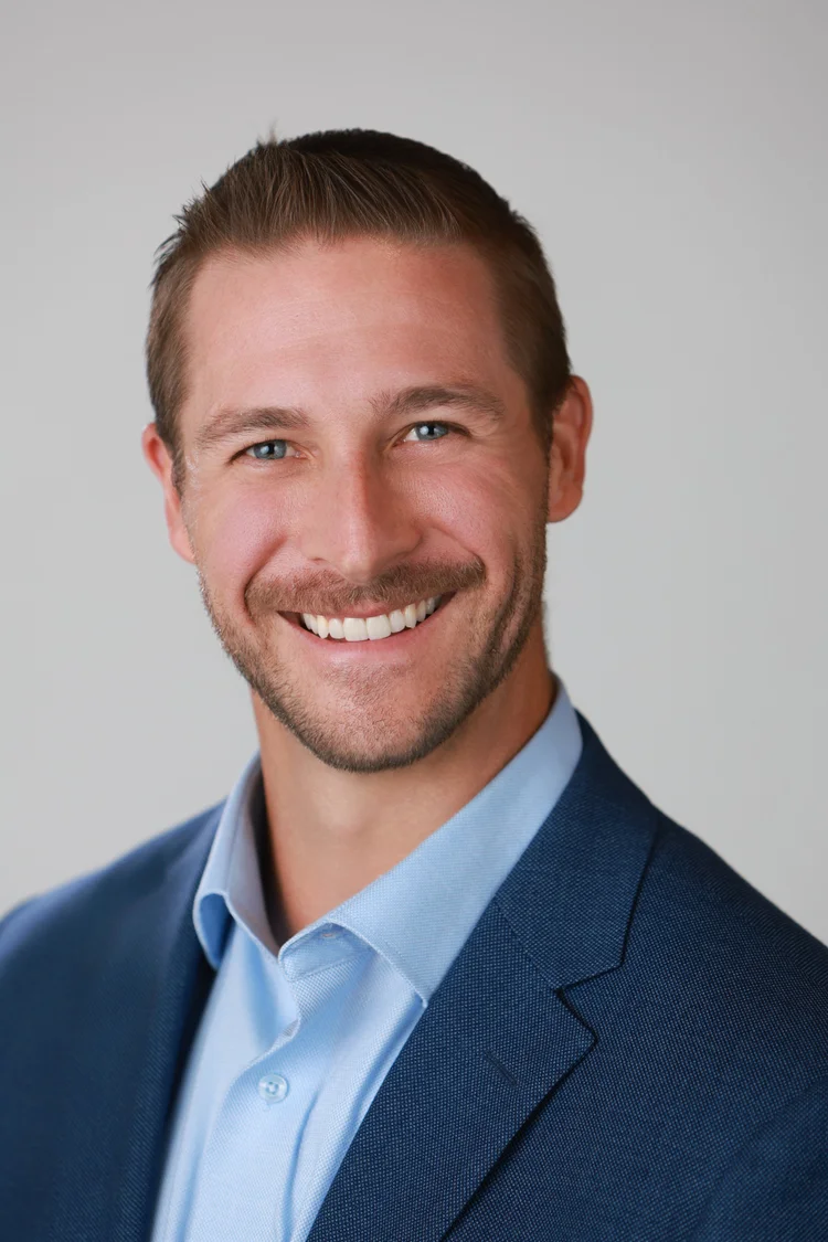 Conference headshot of a man in a navy blazer on a gray backdrop, photographed by Big Wave Productions