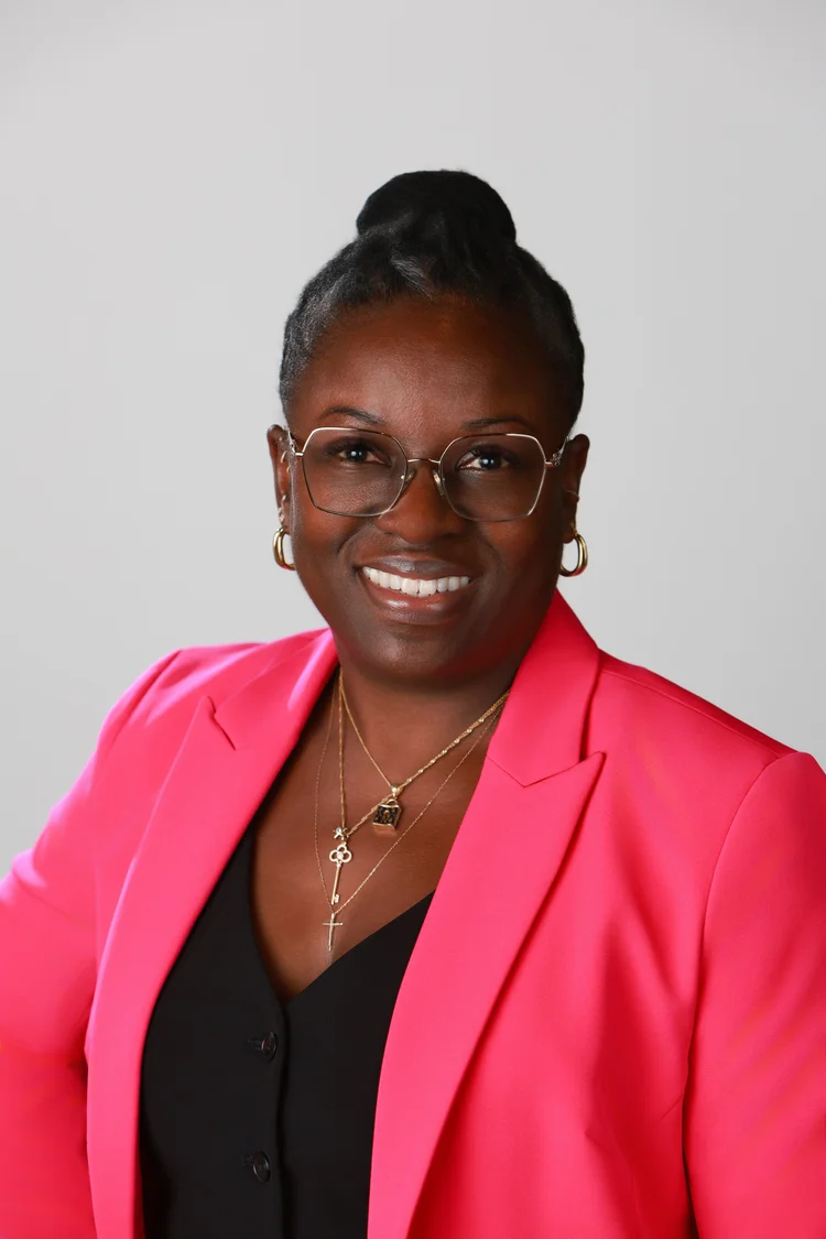Conference headshot of a woman in a pink blazer on a gray backdrop, photographed by Big Wave Productions