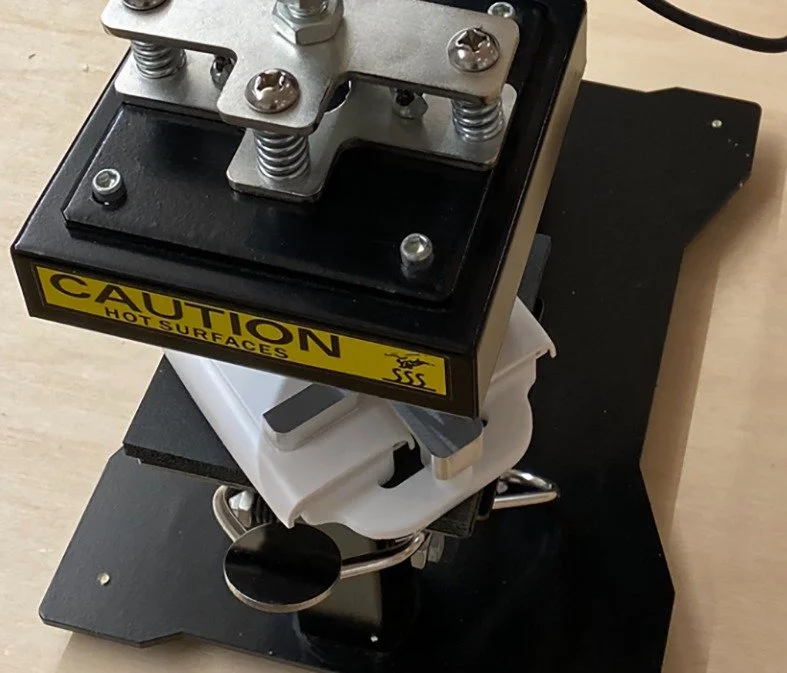 Laboratory magnet or machine with a caution sticker, metal components, and a white plastic part on a black base.