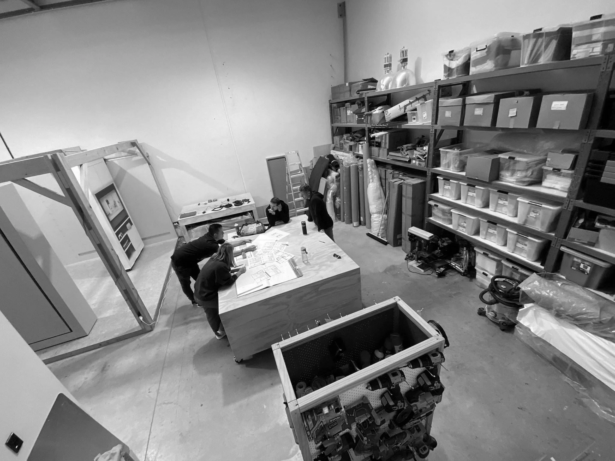 People working in a storage room or warehouse with shelves filled with boxes and containers.