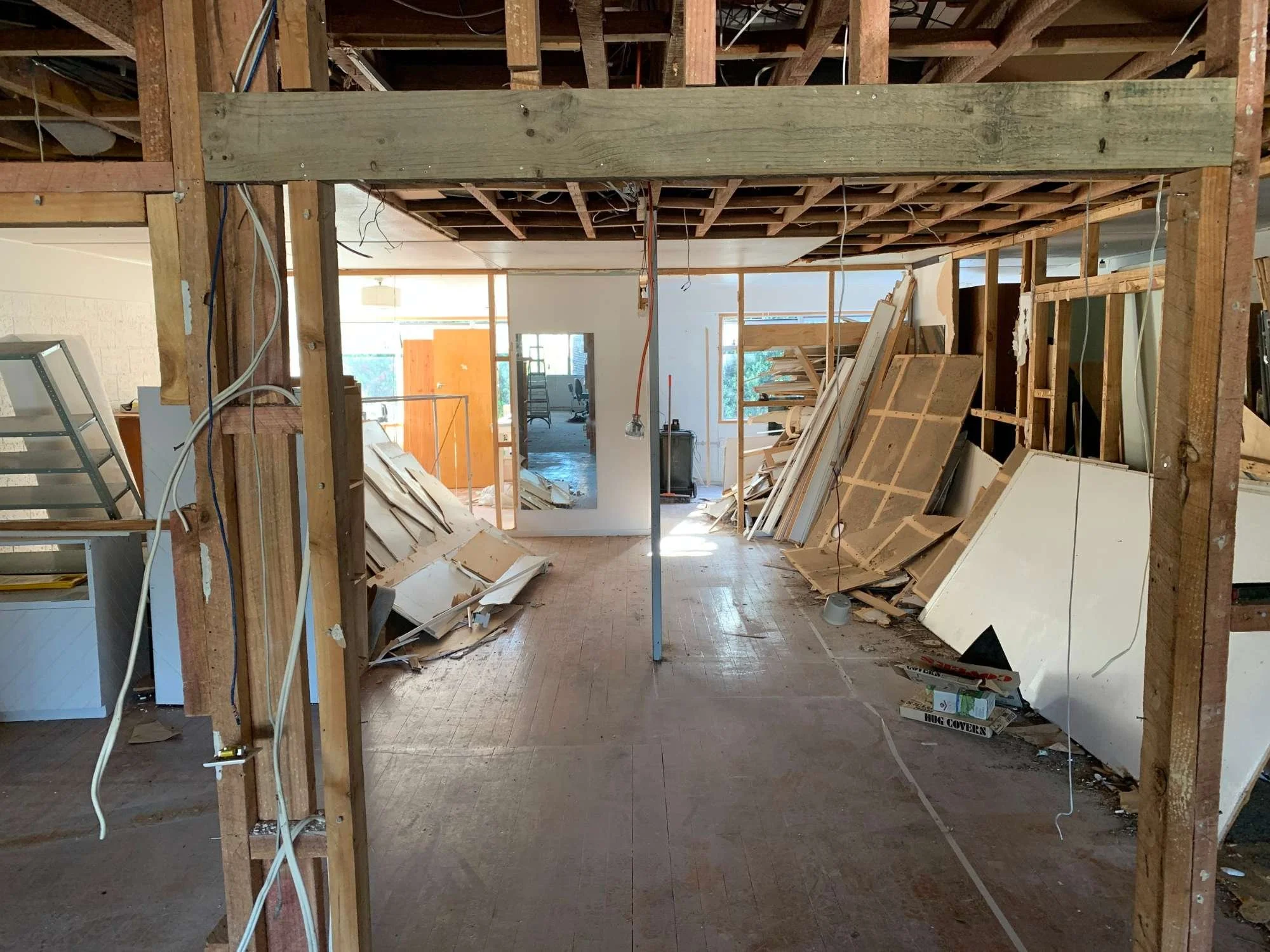 Interior view of a house under renovation with exposed wooden framing, construction debris, and unfinished spaces.