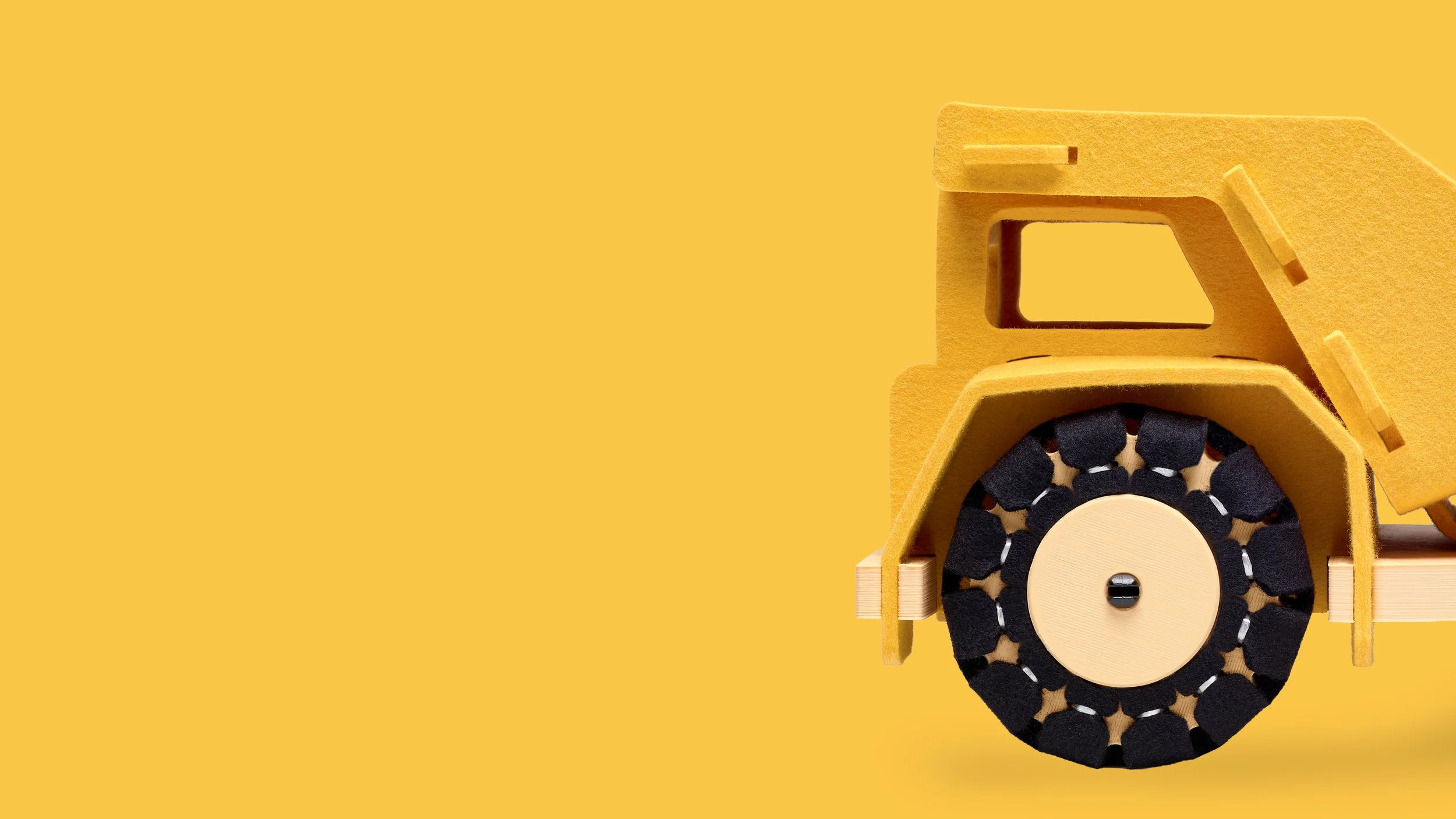 Close-up of a yellow wooden woolkin toy truck with black wheels on a yellow background.