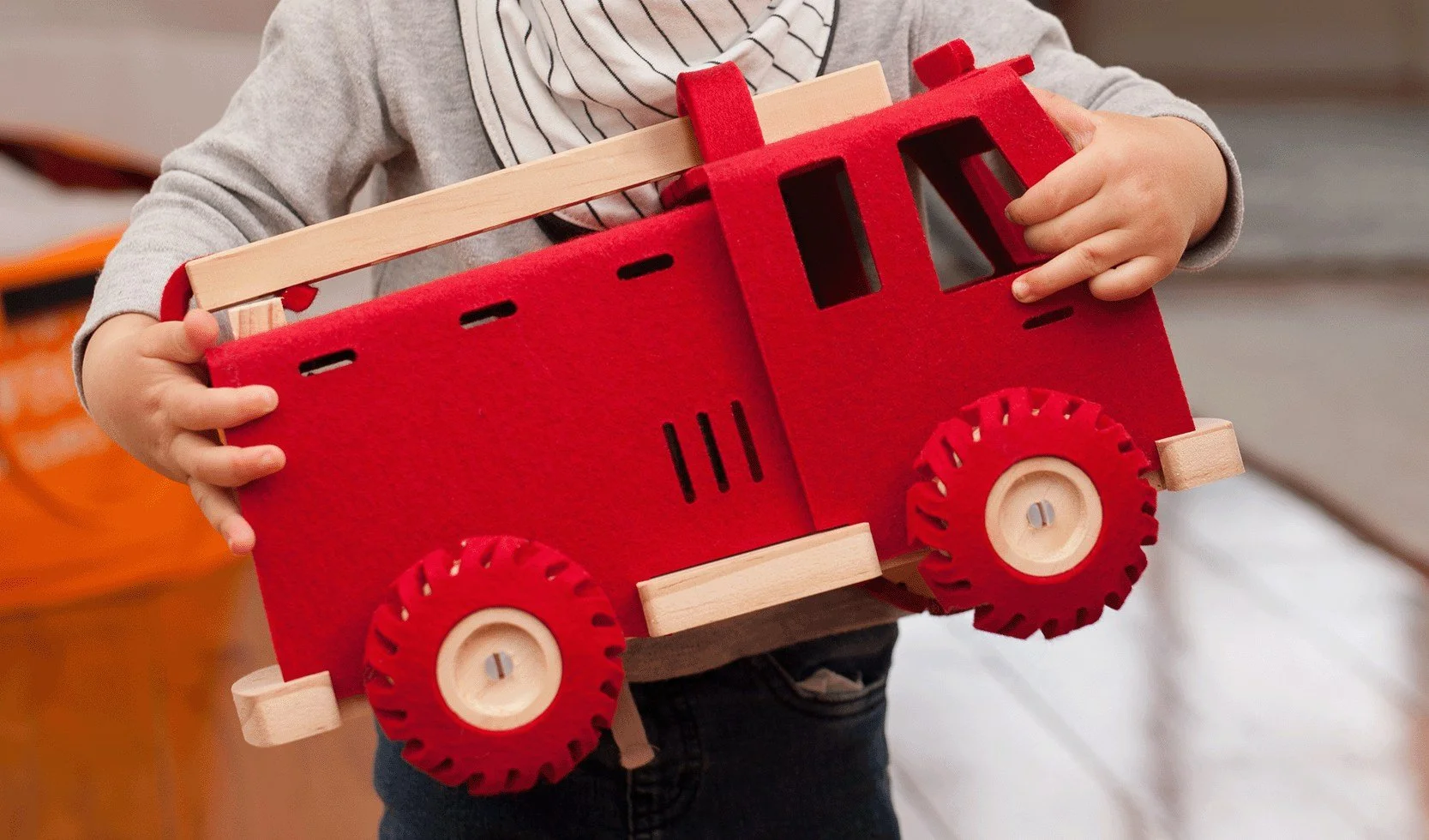 Child holding a red and wooden toy truck with large red wheels.