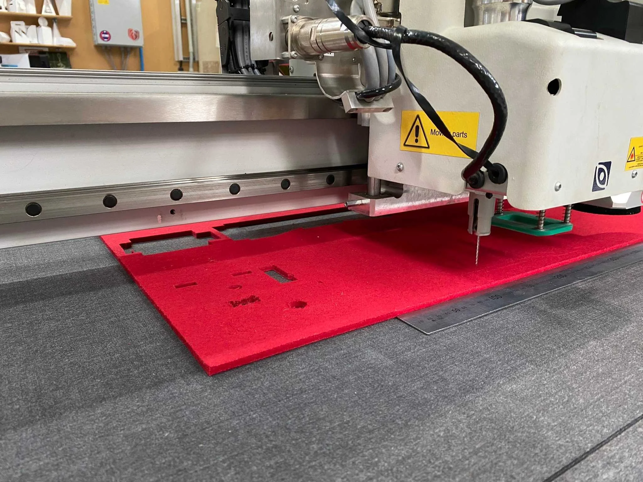 Close-up of a laser engraving machine with a red carpet underneath, showing the machine's components and wiring, set in a workshop environment.