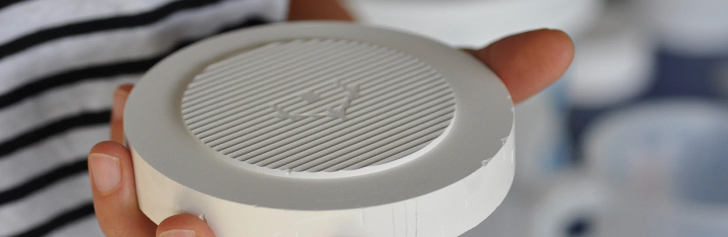 A person holding a white round object with a ribbed surface and a logo in the center.