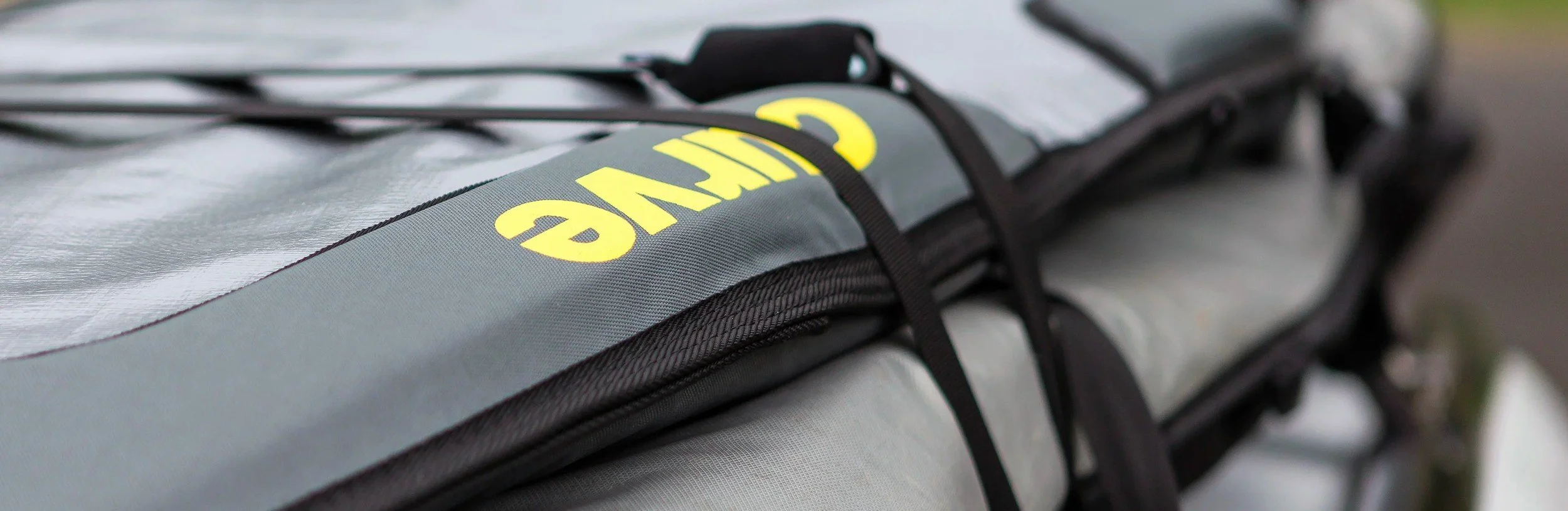 Close-up of a rolled-up black and gray kayak or paddleboard with yellow lettering and secured with black straps.