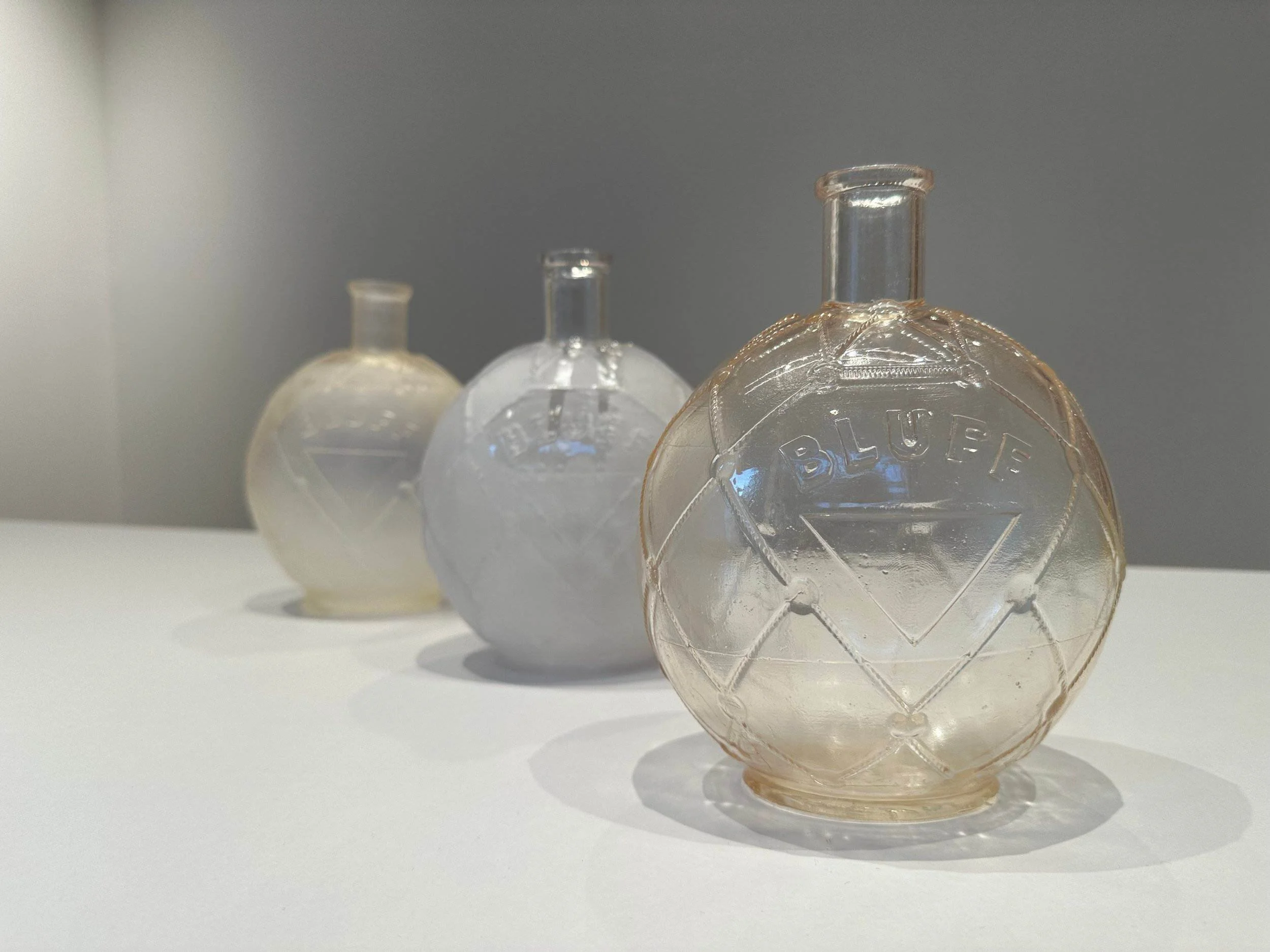 Close-up of three glass soda bottles with embossed labels, positioned on a white surface against a gray background.