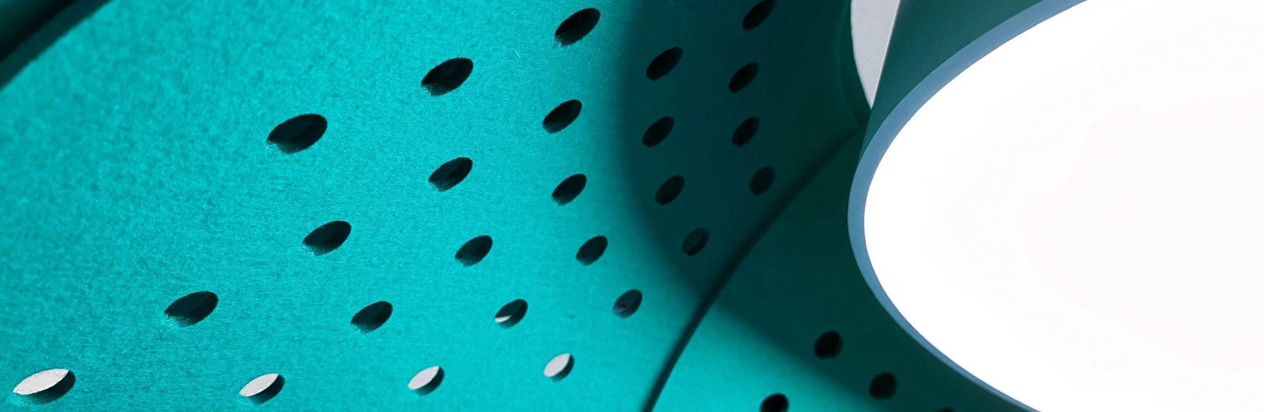 Close-up of a teal-colored shower head with oval holes.