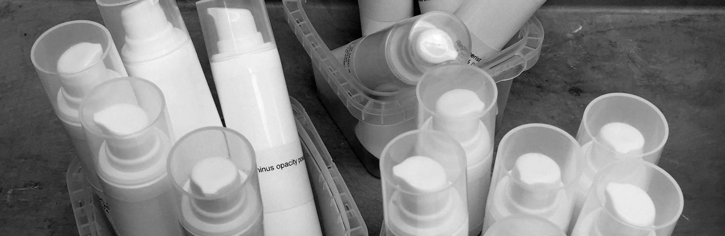 Several bottles of skincare or cosmetic products with flip-top caps on a wooden surface, some in plastic containers and trays.