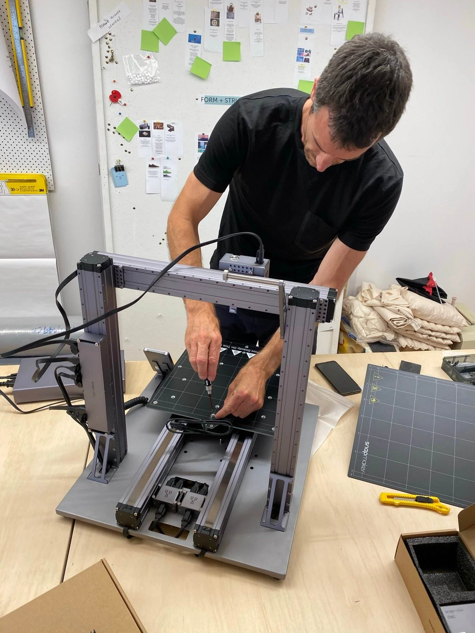 A person operating a CNC machine at a workspace with tools, cutting mats, and paper on a table.