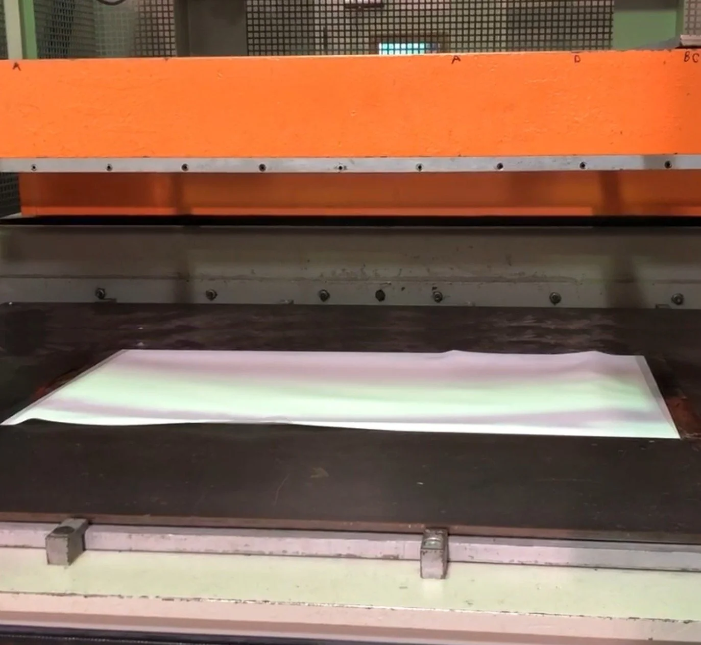 A lightbox displaying a white sheet of paper with some green on it, under an orange heated press.