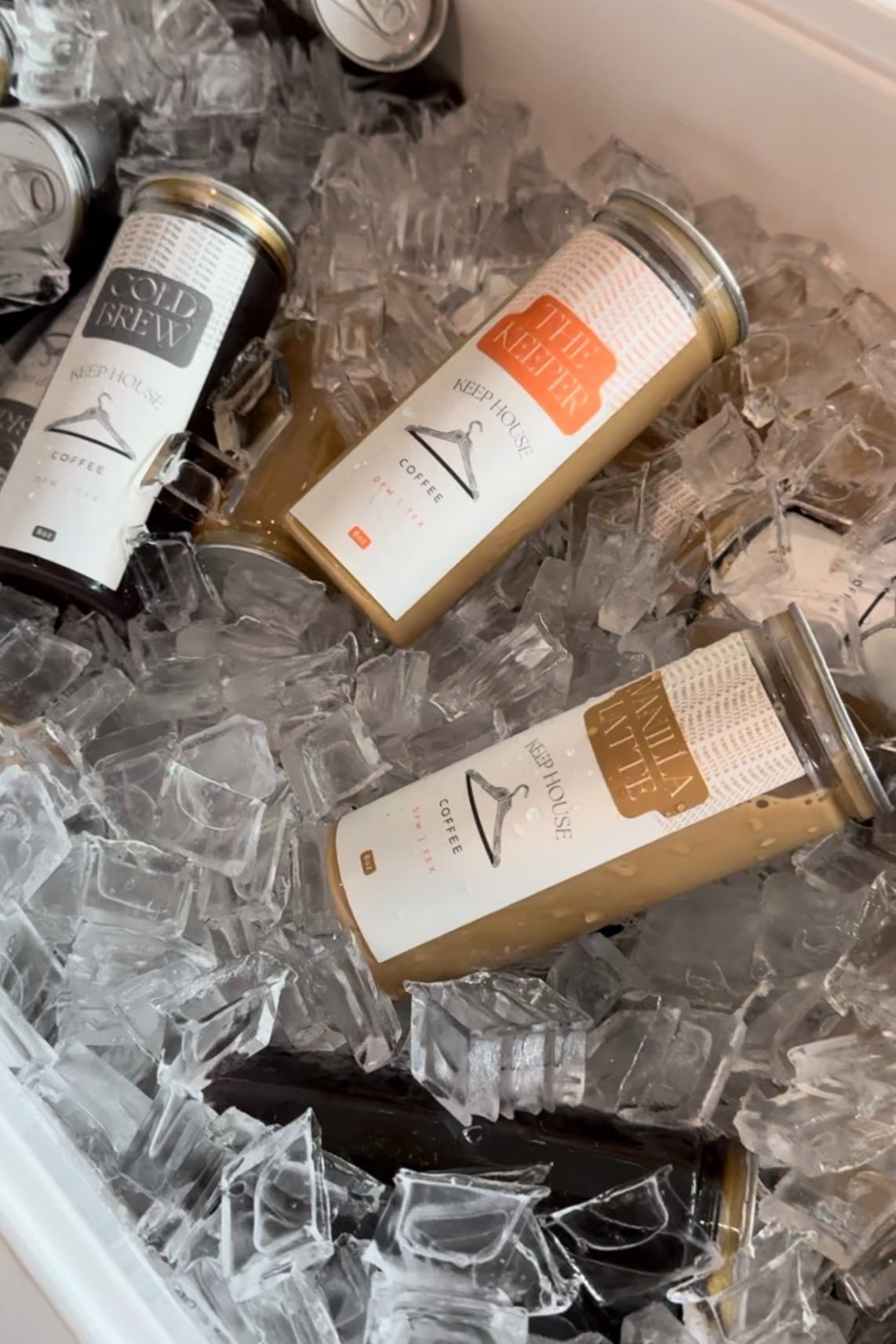 Three cans of Keep House coffee on ice in a cooler, surrounded by crushed ice.