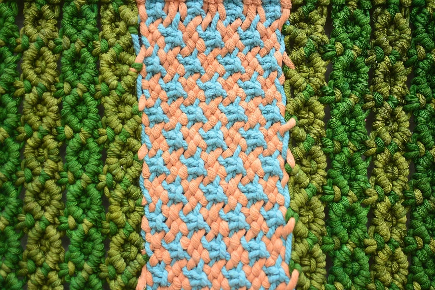 Textura de tejido con hilos verdes y un patrón azul y rosa en medio.