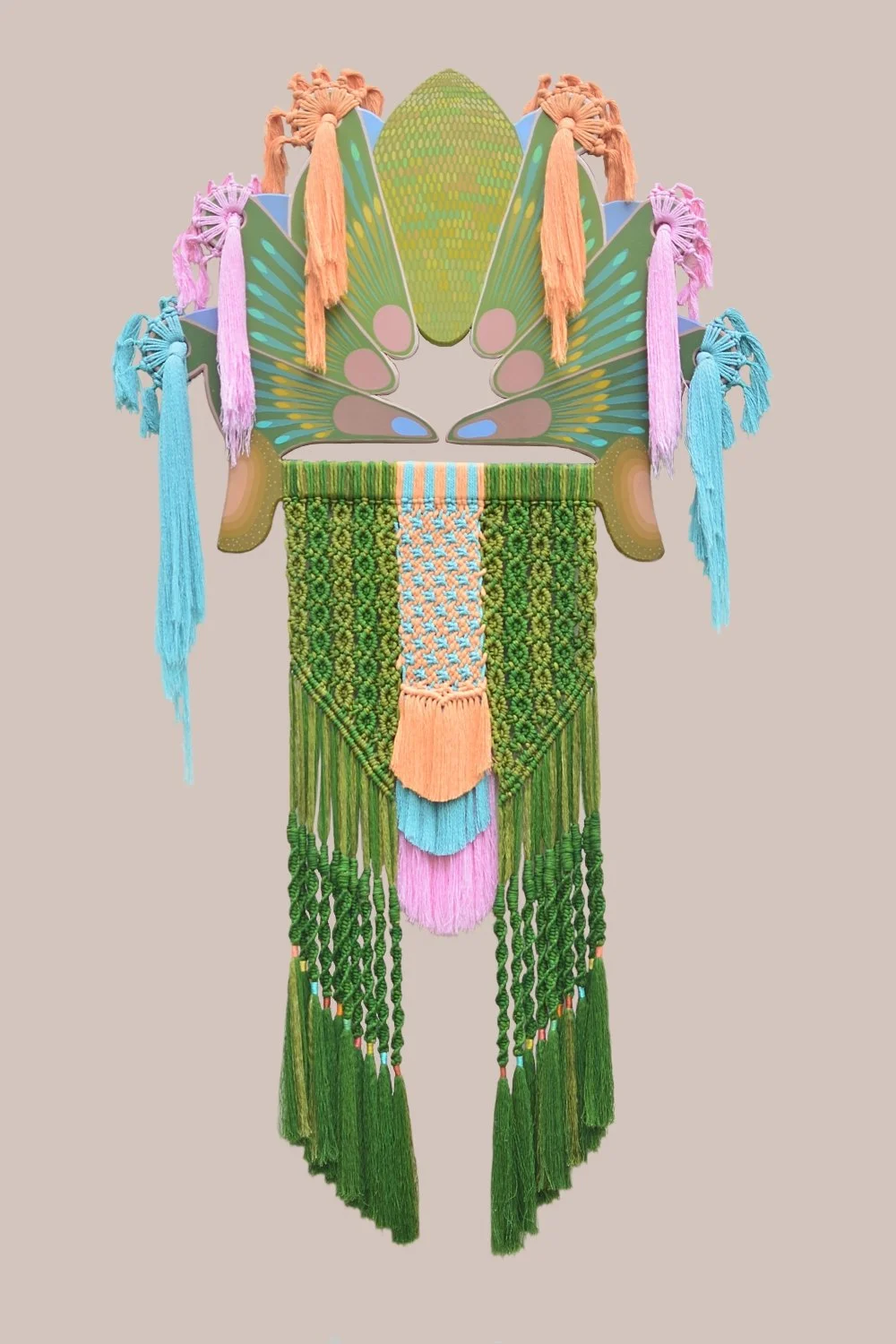 Decoración colorida con elementos de textiles y madera, en tono verde, rosado, azul y naranja, en forma de manto y colgantes estilo artesanal.