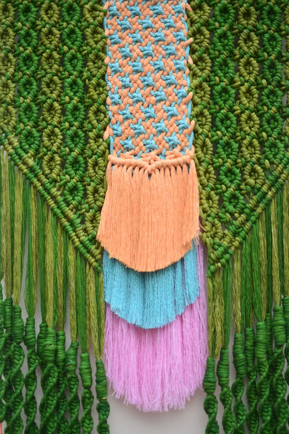Textiles artesanales con hilos de color verde, naranja, azul y rosa, decorados con flecos.