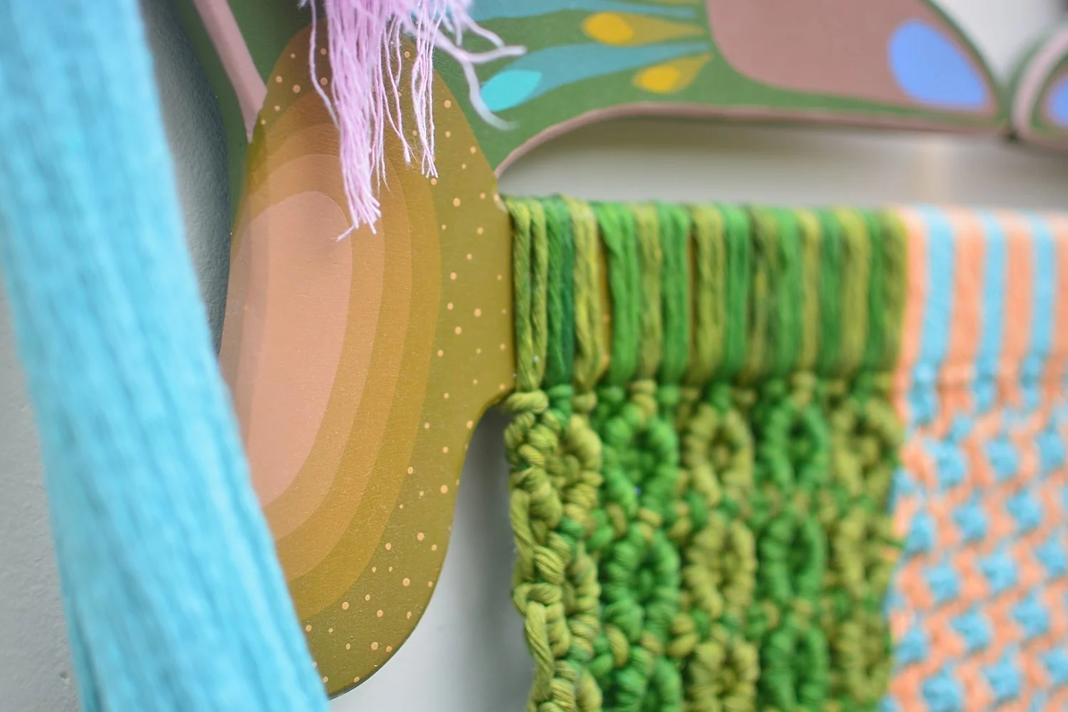 Detalles de arte textil en coloridos hilos y telas en tonos verdes, azules y naranjas en una estructura decorativa.