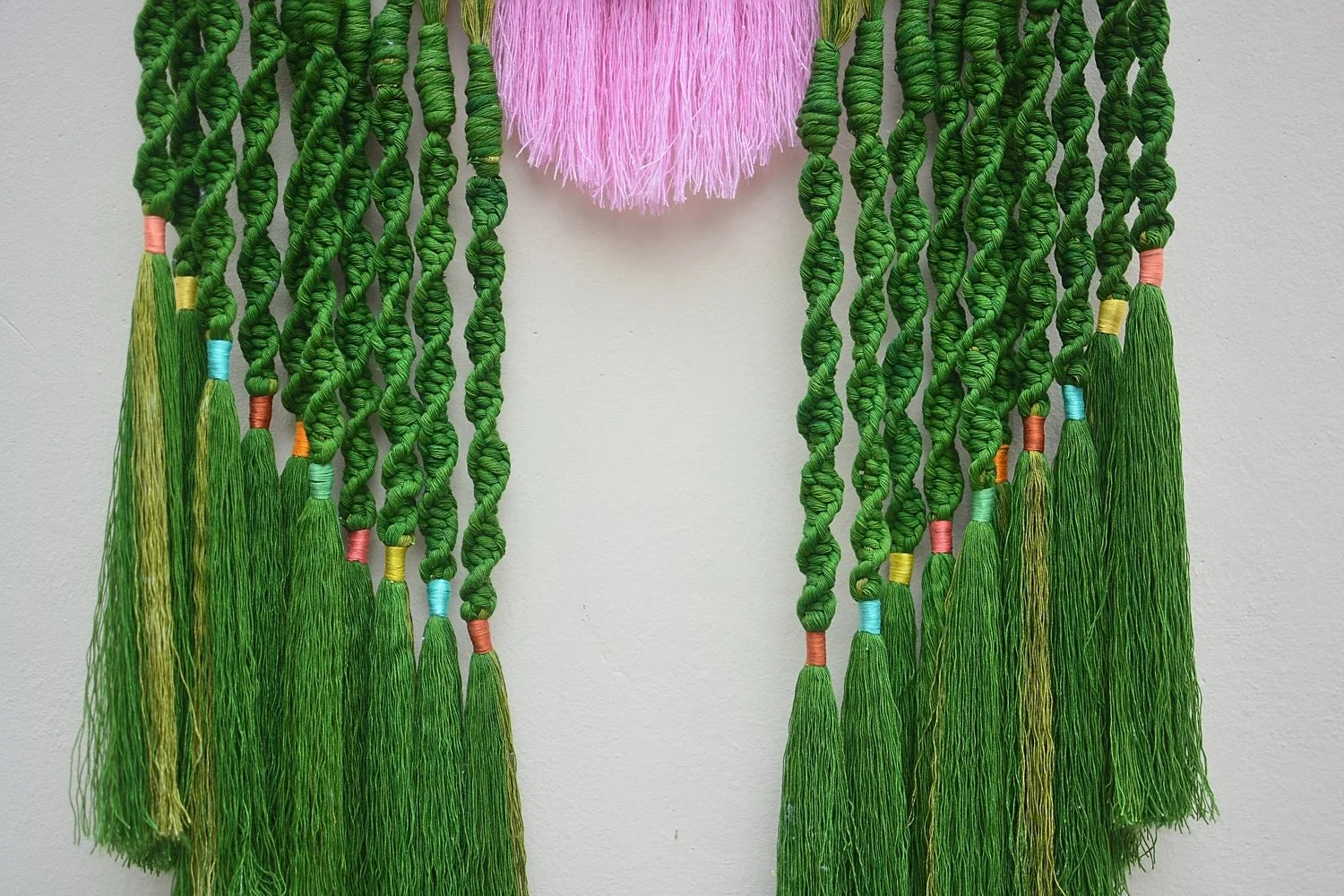 Decoración con hilos verdes, trenzados y sueltos, adornados con pequeños lazos de colores, colgados en una pared