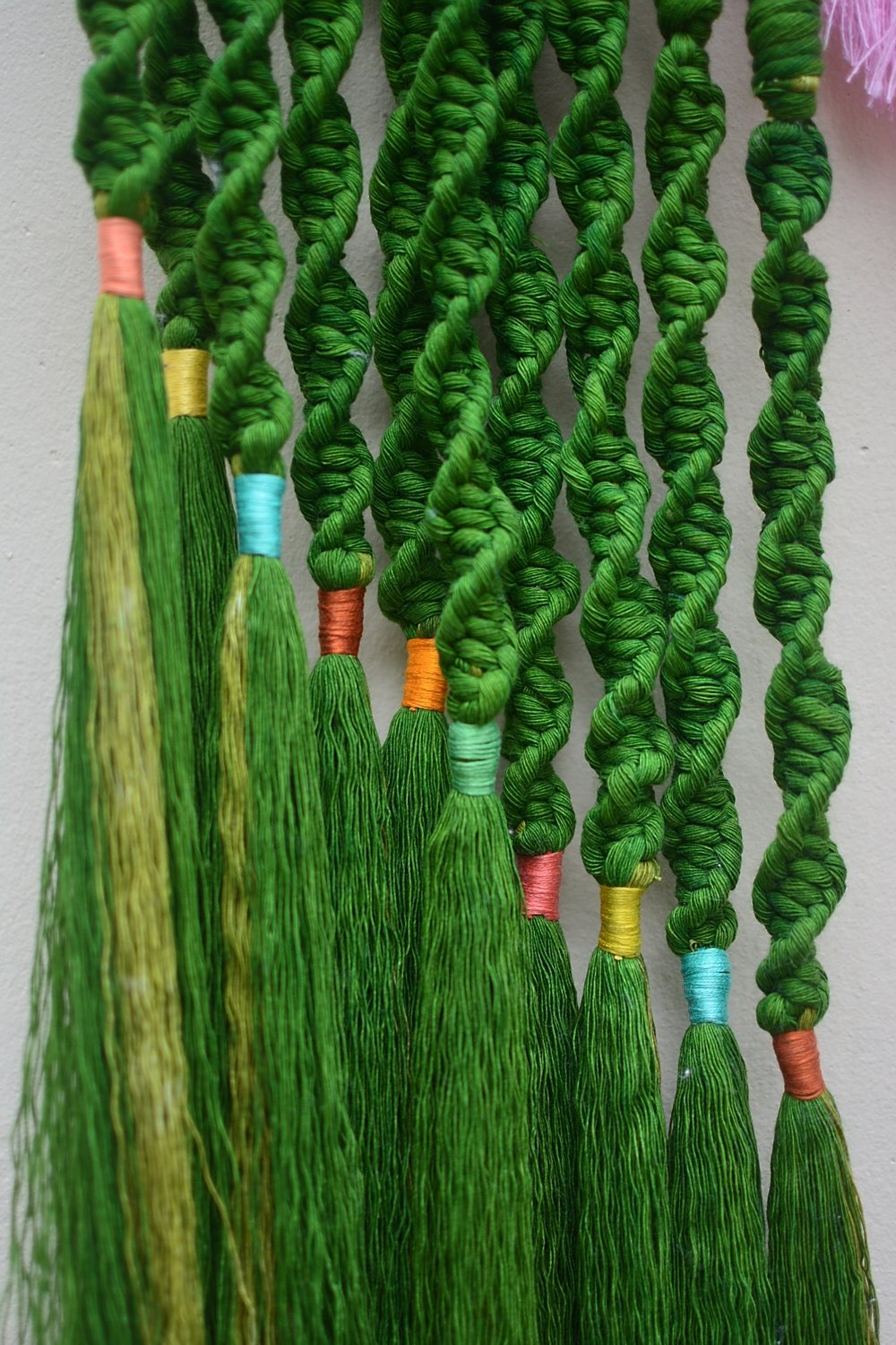 Hilos de hilados verdes con algunos con puntas envueltas en diferentes colores, colgados en una pared.