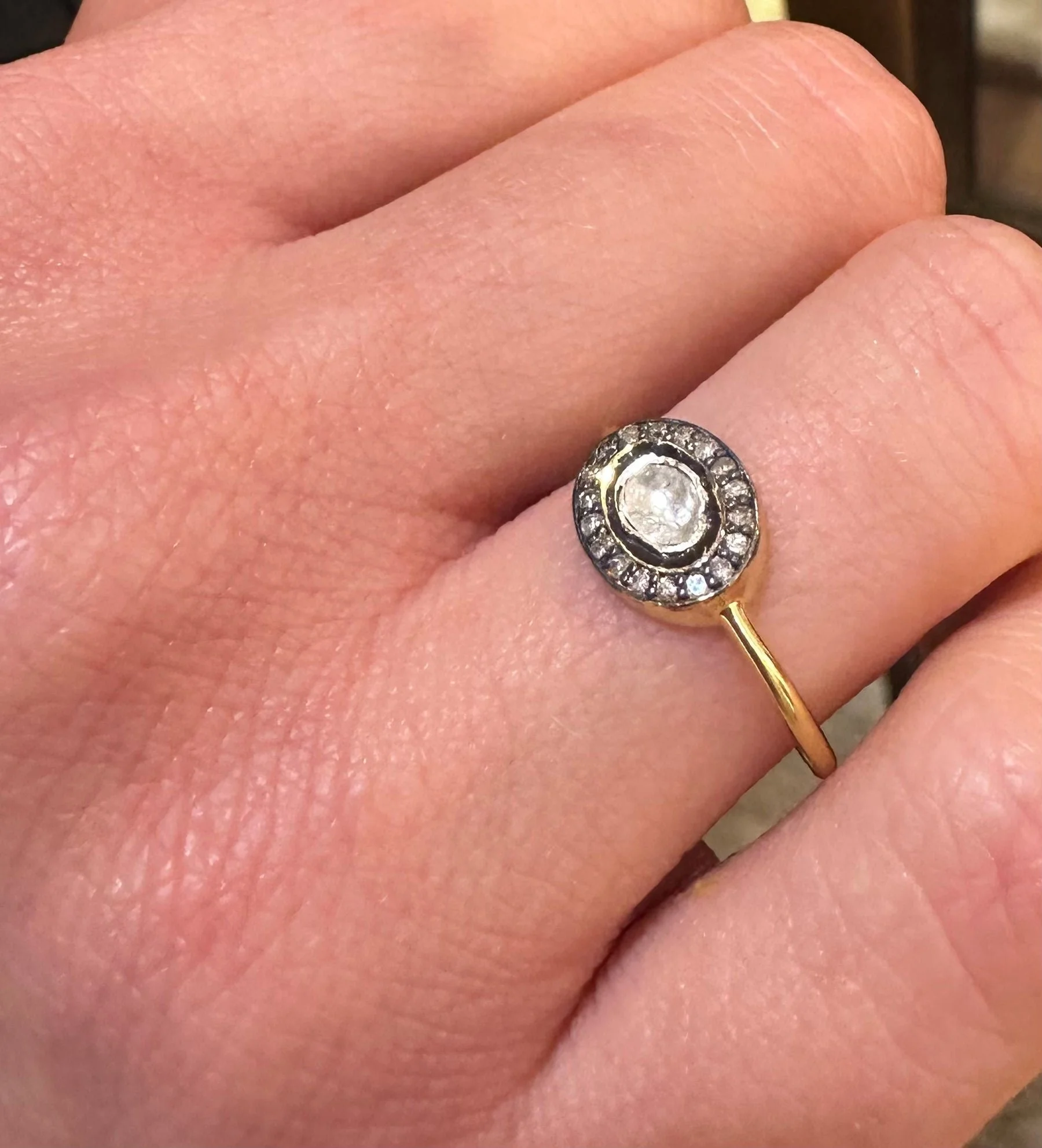 A gold ring with a center diamond surrounded by smaller diamonds, worn on a person's finger.