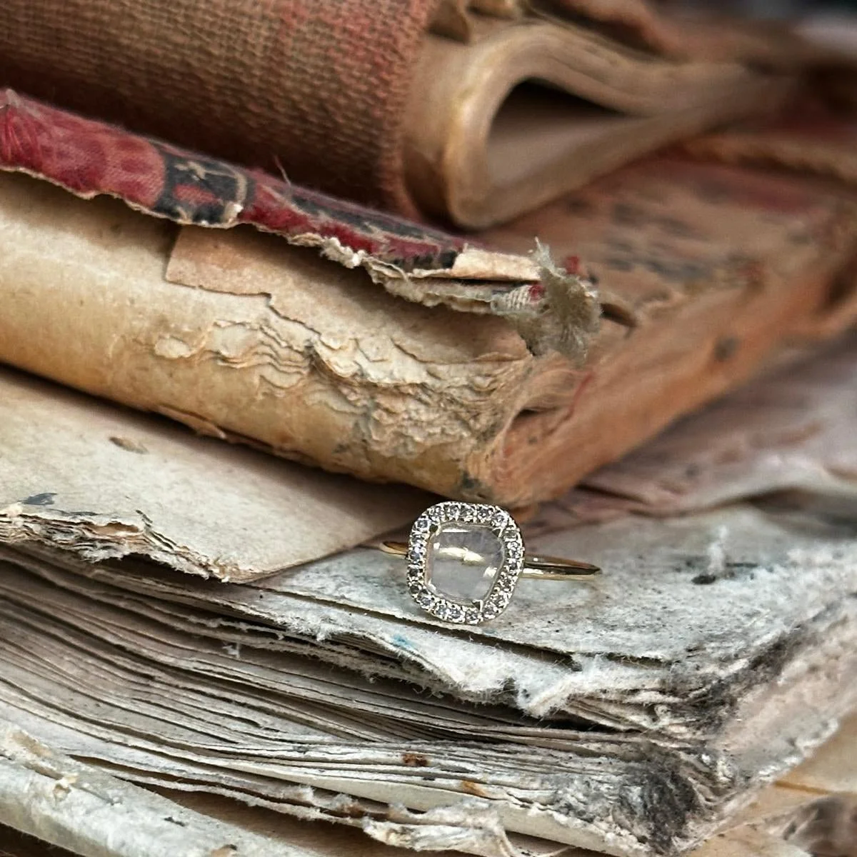 A diamond ring resting on aged, weathered papers with old books stacked behind it.