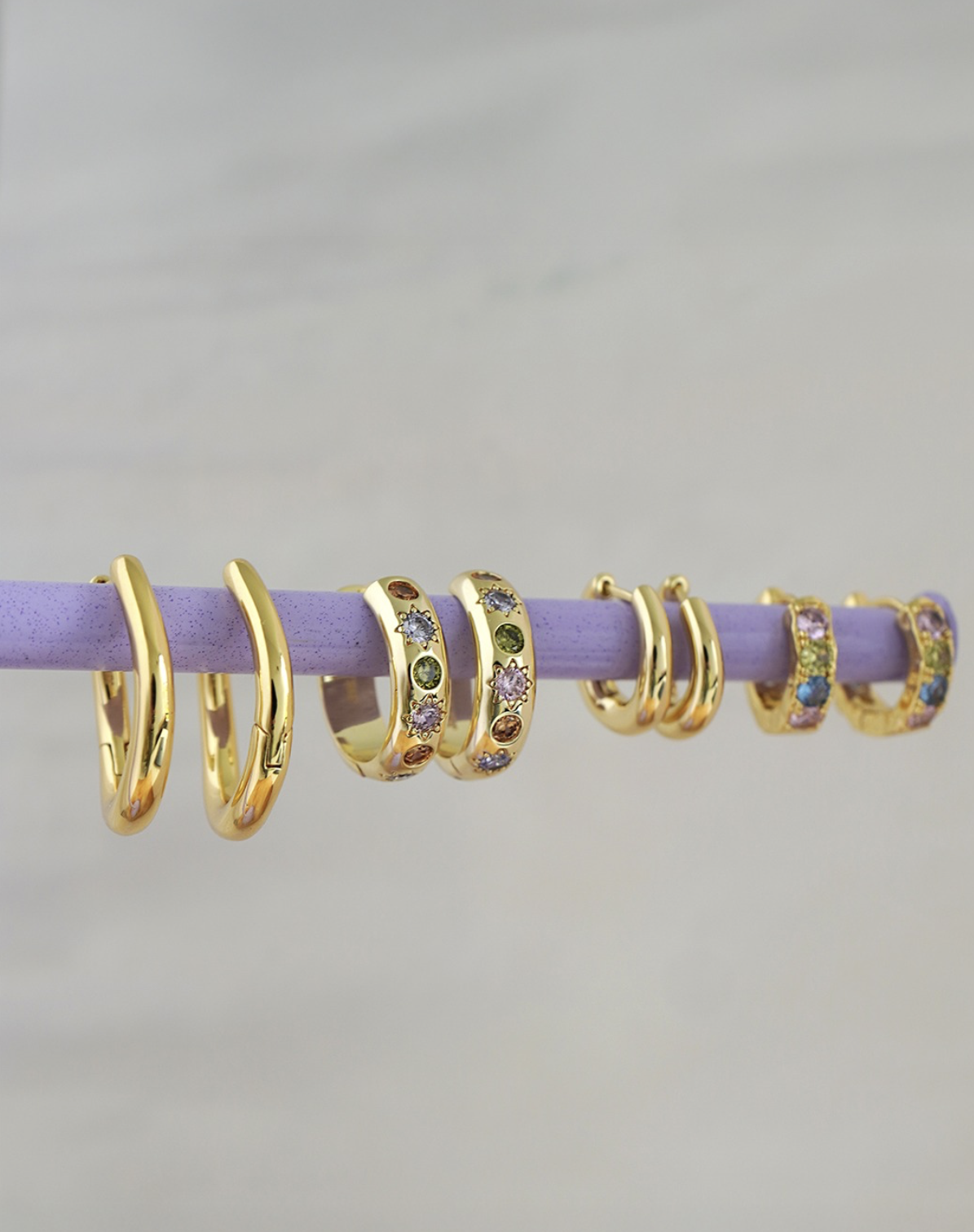 Several gold rings with colorful gemstones hanging on a lavender-colored rod.